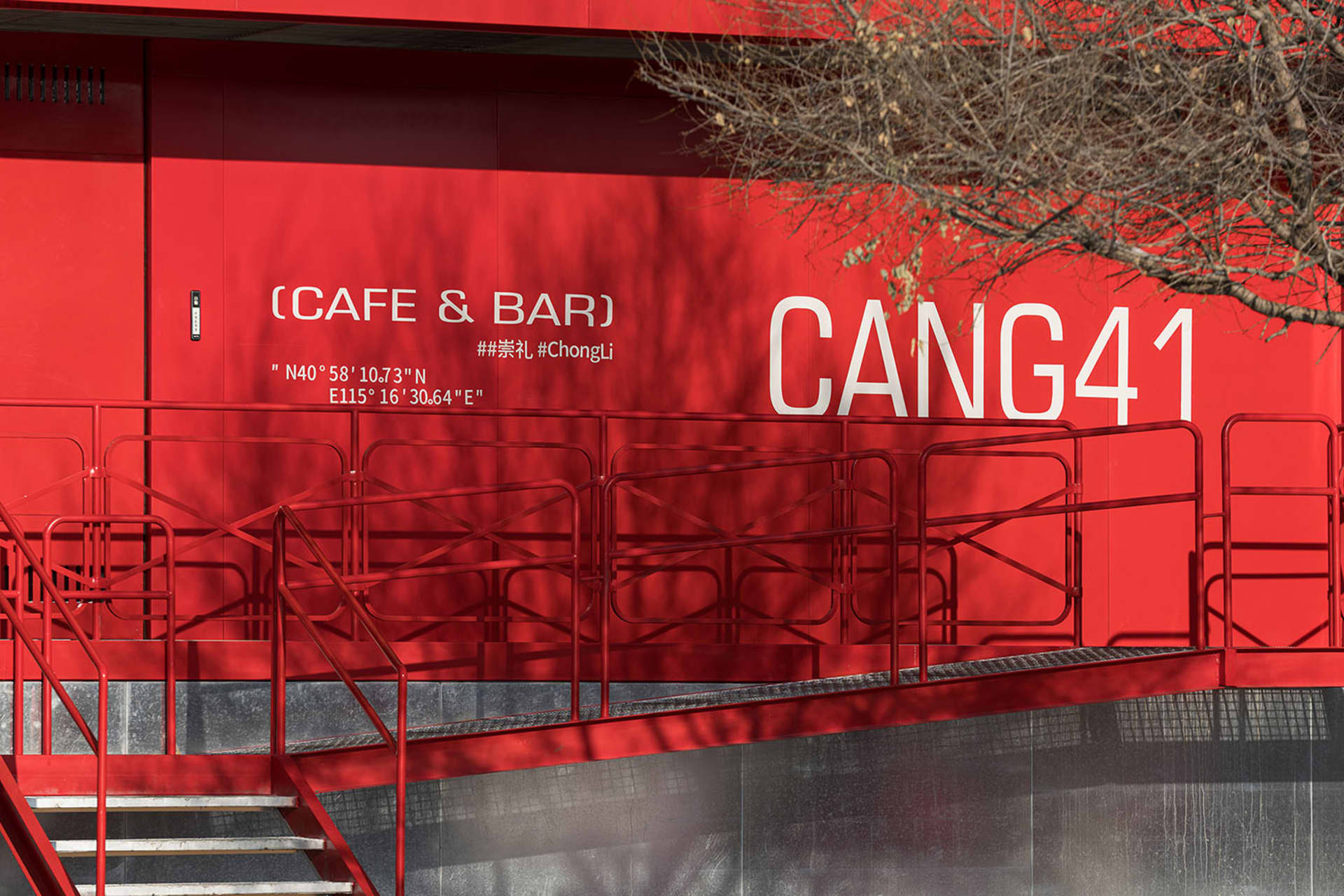 A red building with a staircase leading to a second floor, featuring railings and a possible restaurant or bar design