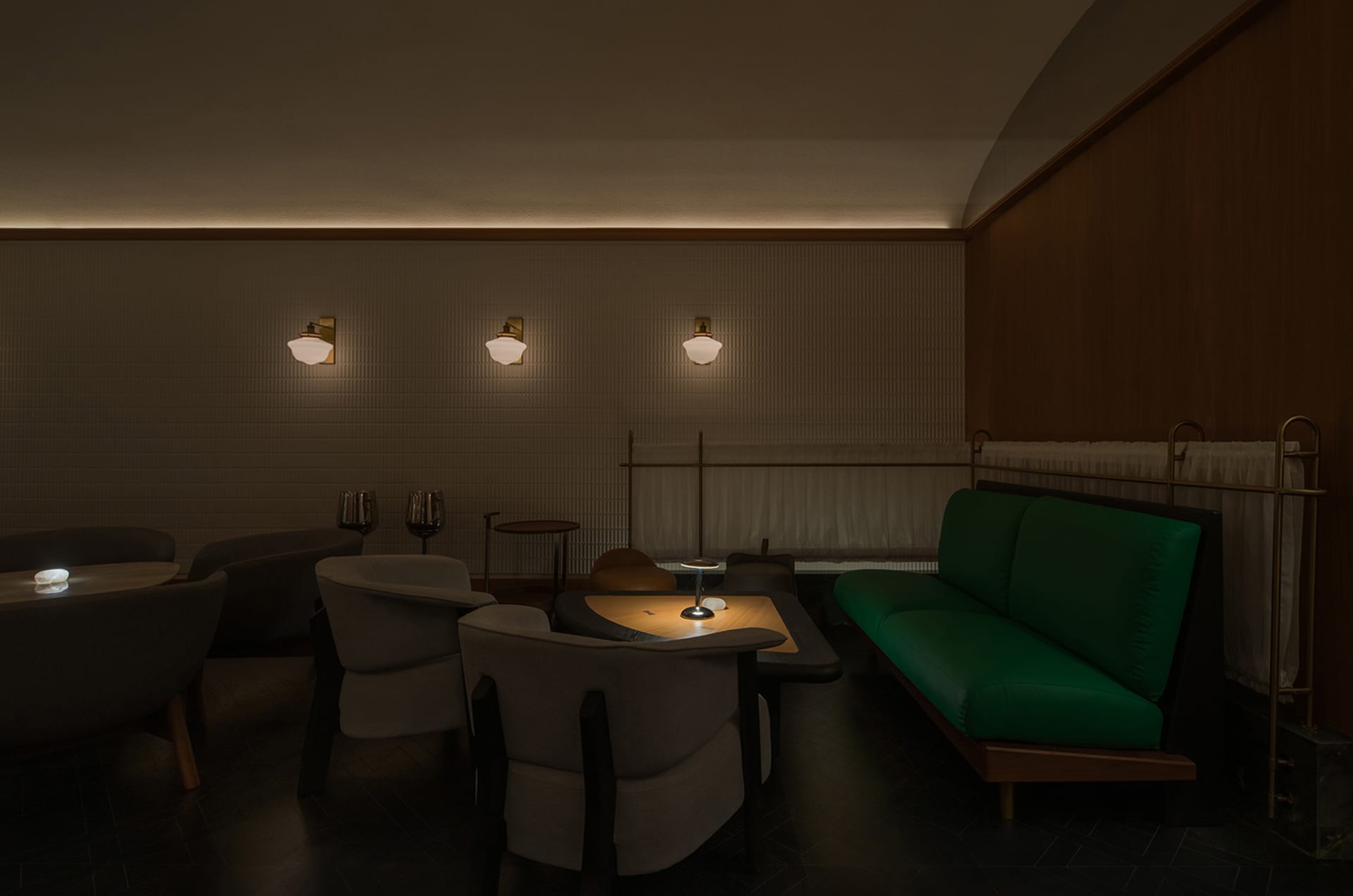 Cozy living room with a green couch, two chairs, a dining table, and a bar area, featuring wine glasses and a comfortable seating arrangement