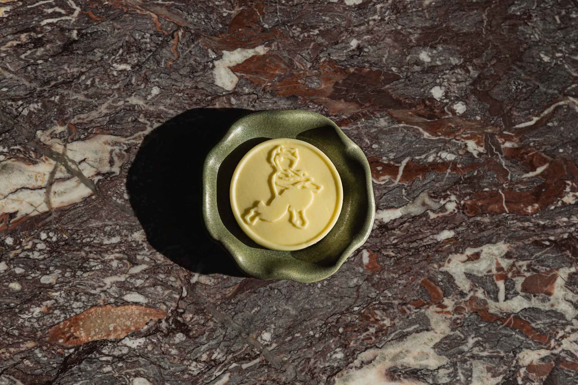 A green ceramic bowl sits on a brown, textured marble countertop with a yellow design in the center of the bowl