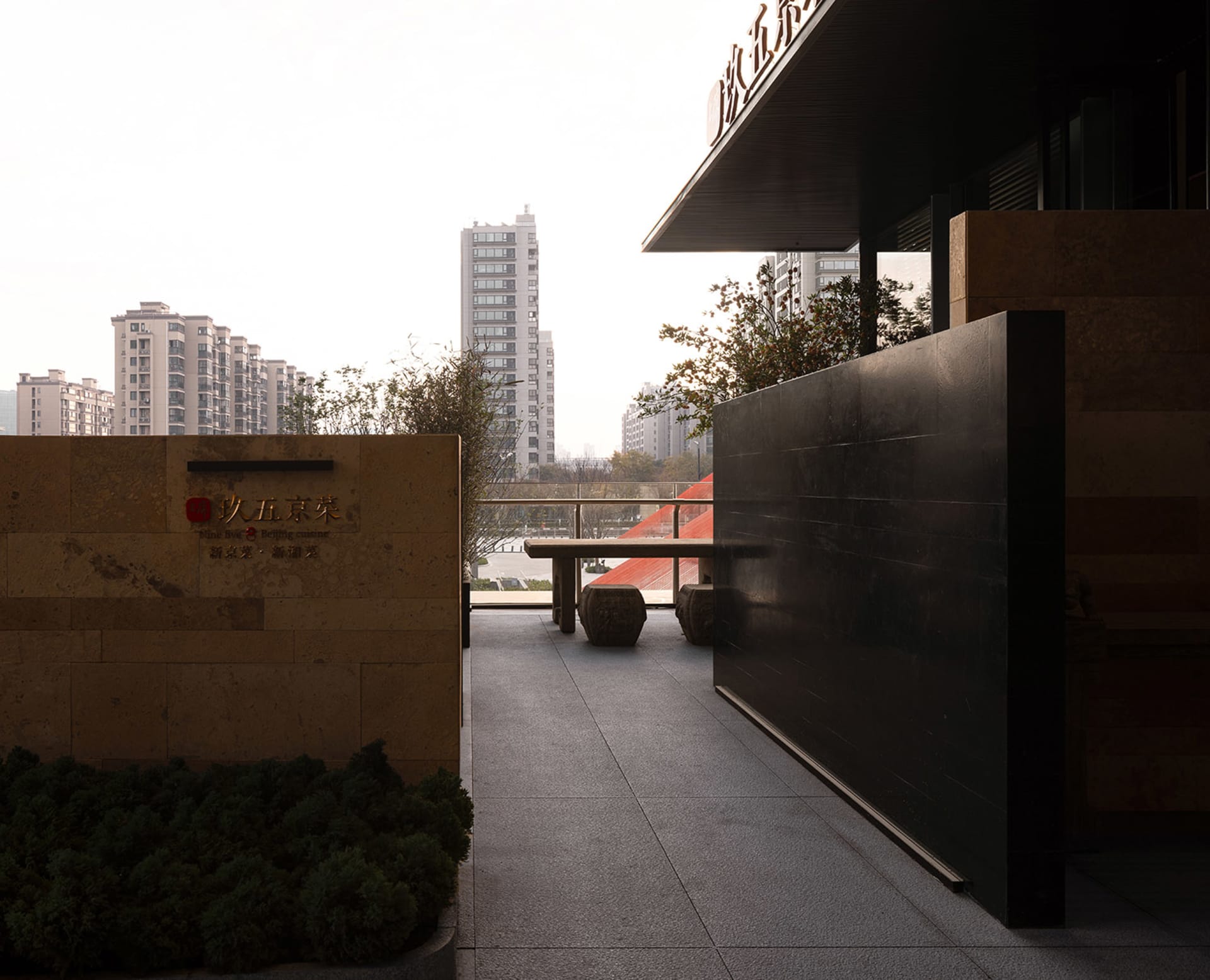 A well-lit balcony with a black doorway, two benches, and a city view through the doorway