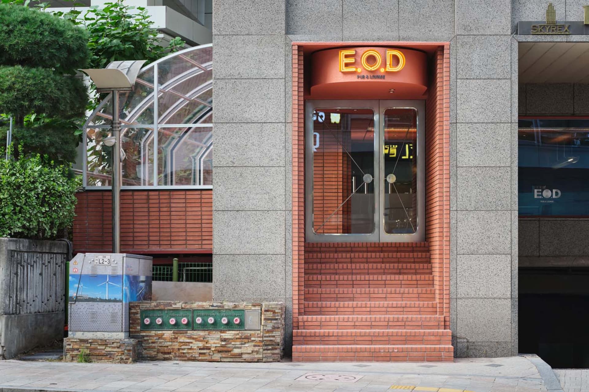 A modern building with a red brick facade, large window, and two doors, set in a contemporary urban environment