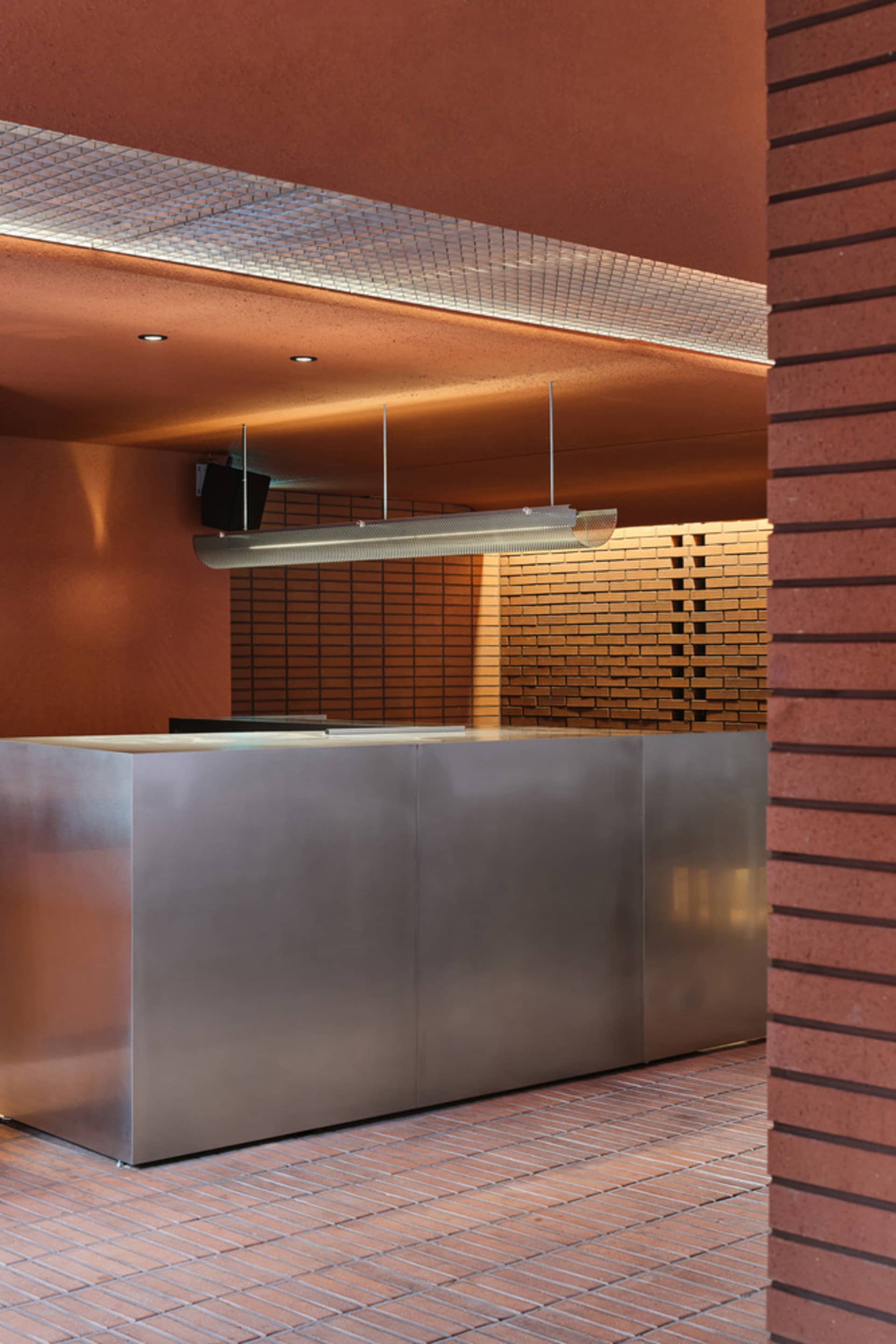 Industrial kitchen with a large silver countertop, two sinks, and a hanging lamp providing illumination