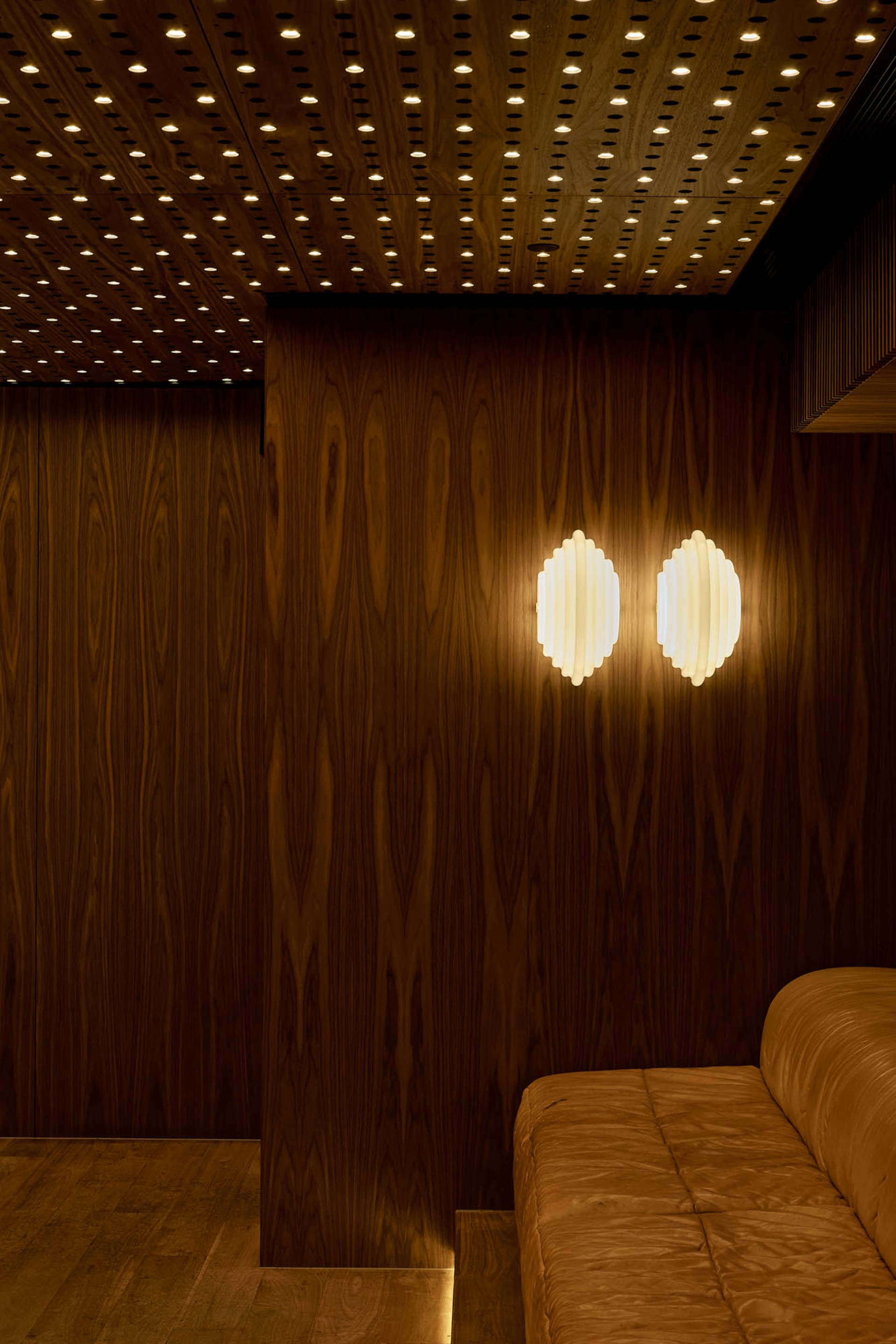 A warm and inviting living area with a brown wooden wall, two wall lights, and a cozy atmosphere