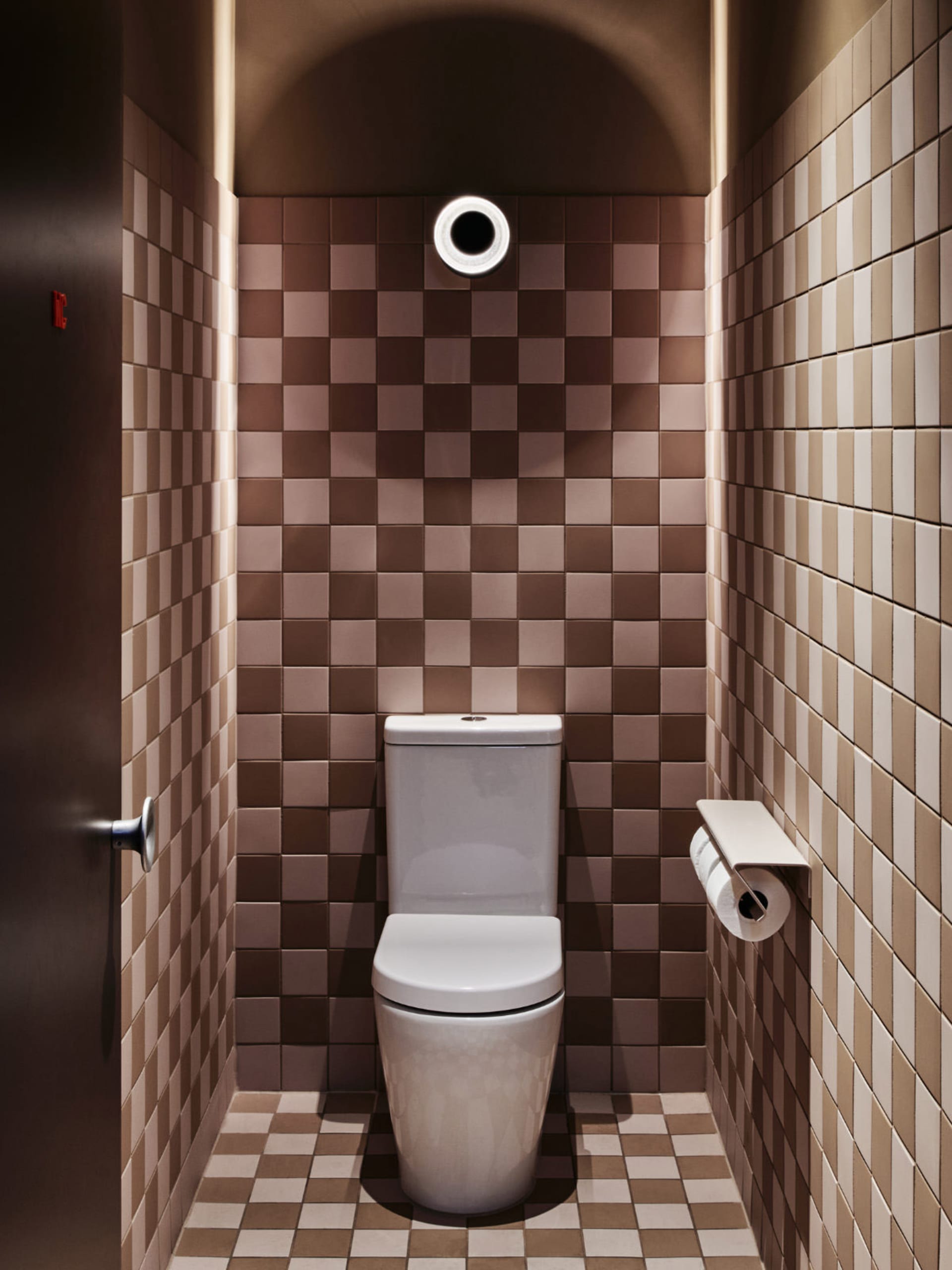 Small bathroom with a white toilet, brown tile walls, and a sink in the background
