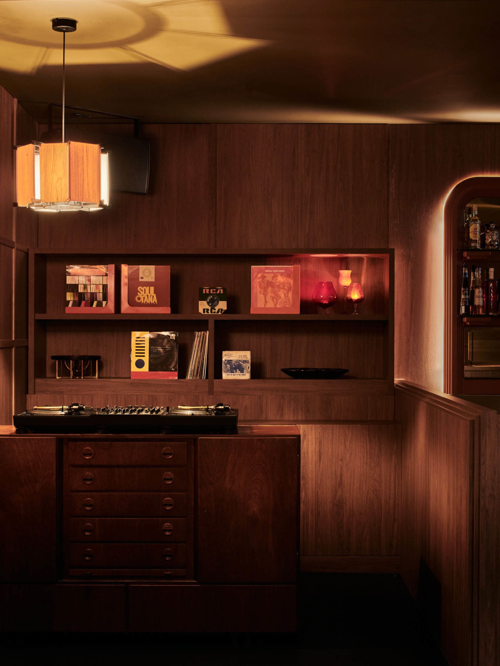 Cozy living space with wooden walls and floors, featuring books, bottles, and a warm atmosphere