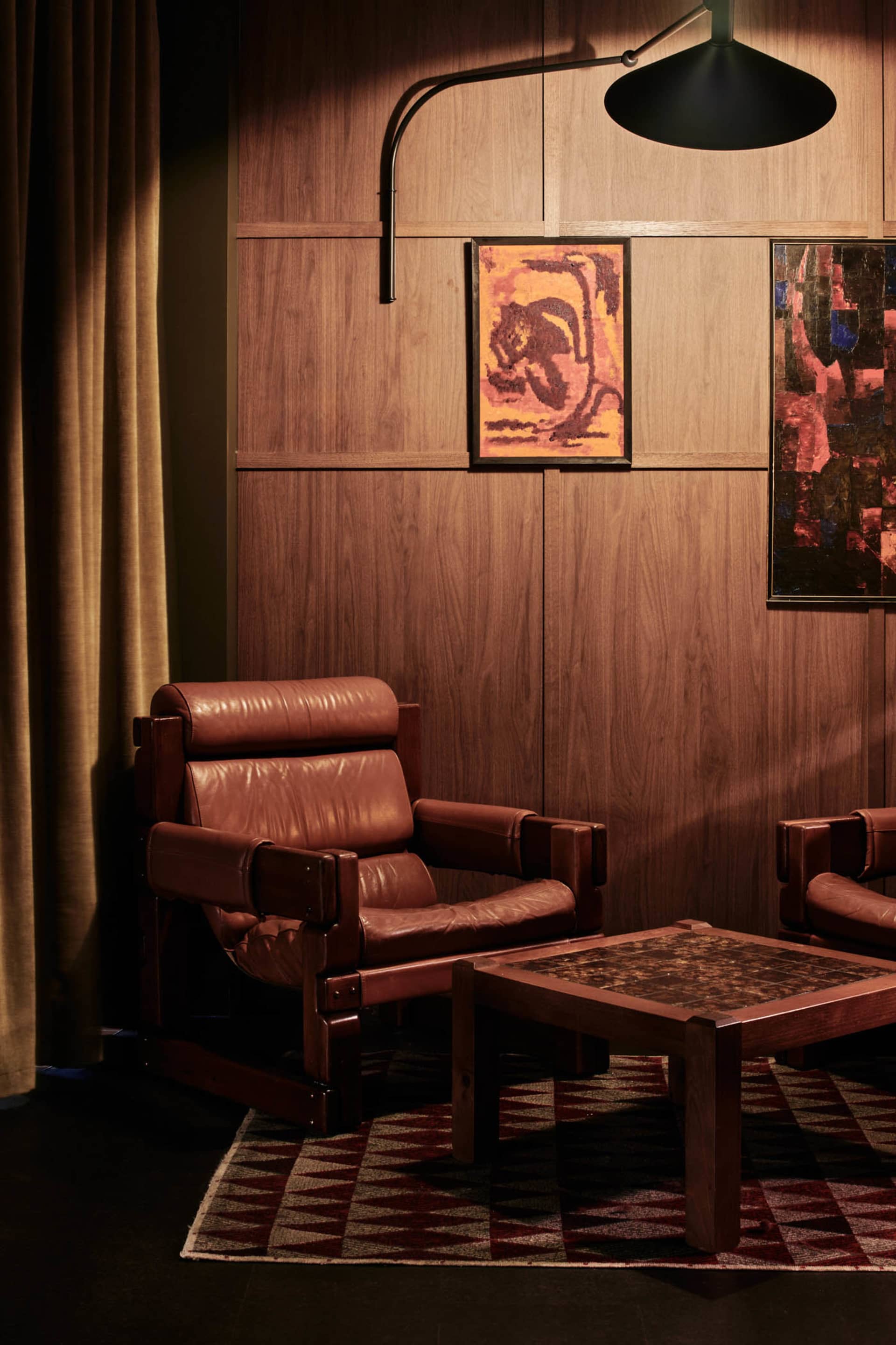 A cozy living room with two leather chairs, a wooden table, and a painting on the wall, creating a warm and inviting atmosphere