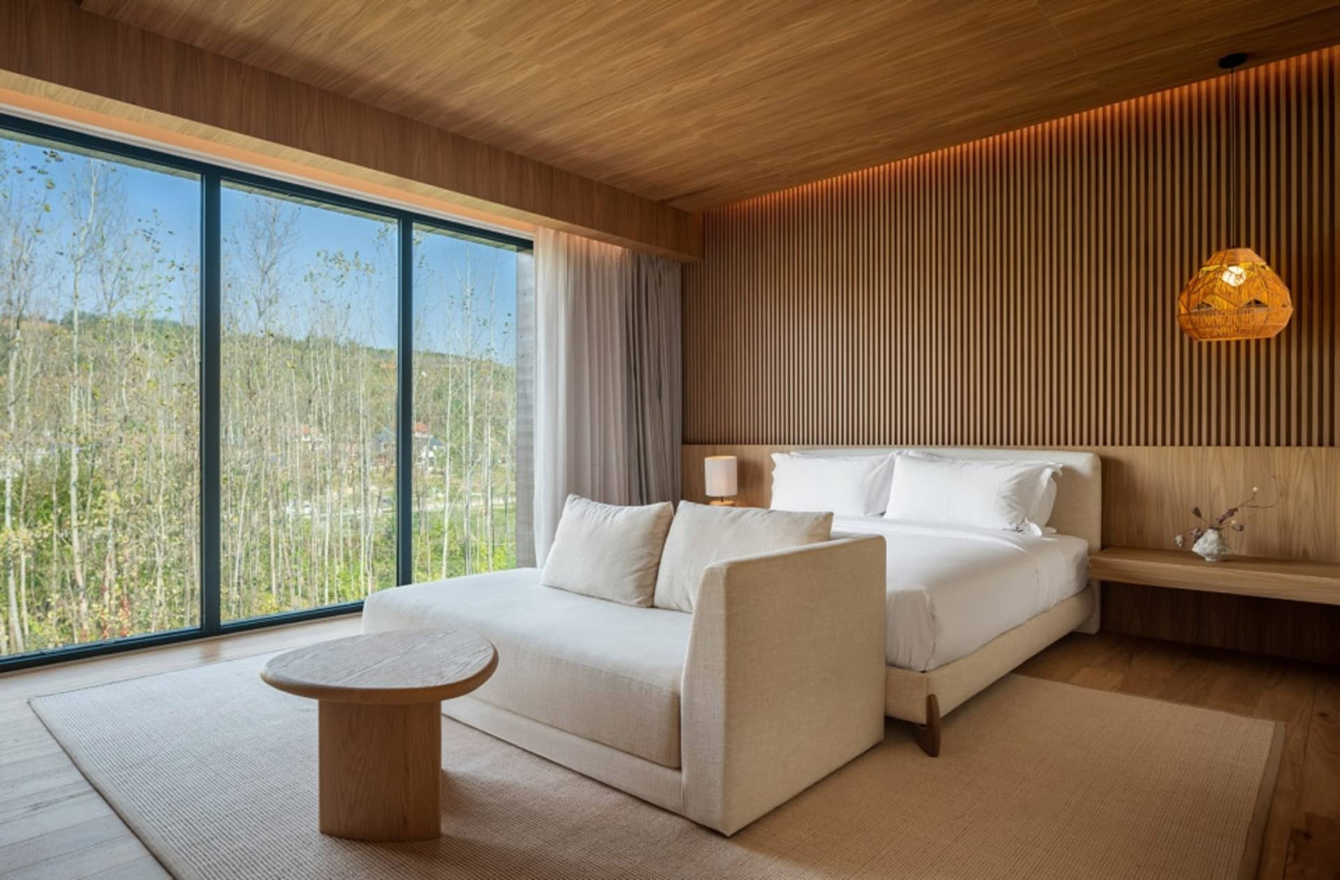 Well-lit bedroom with a large window, a bed, two couches, a chair, and a dining table, creating a modern and inviting atmosphere