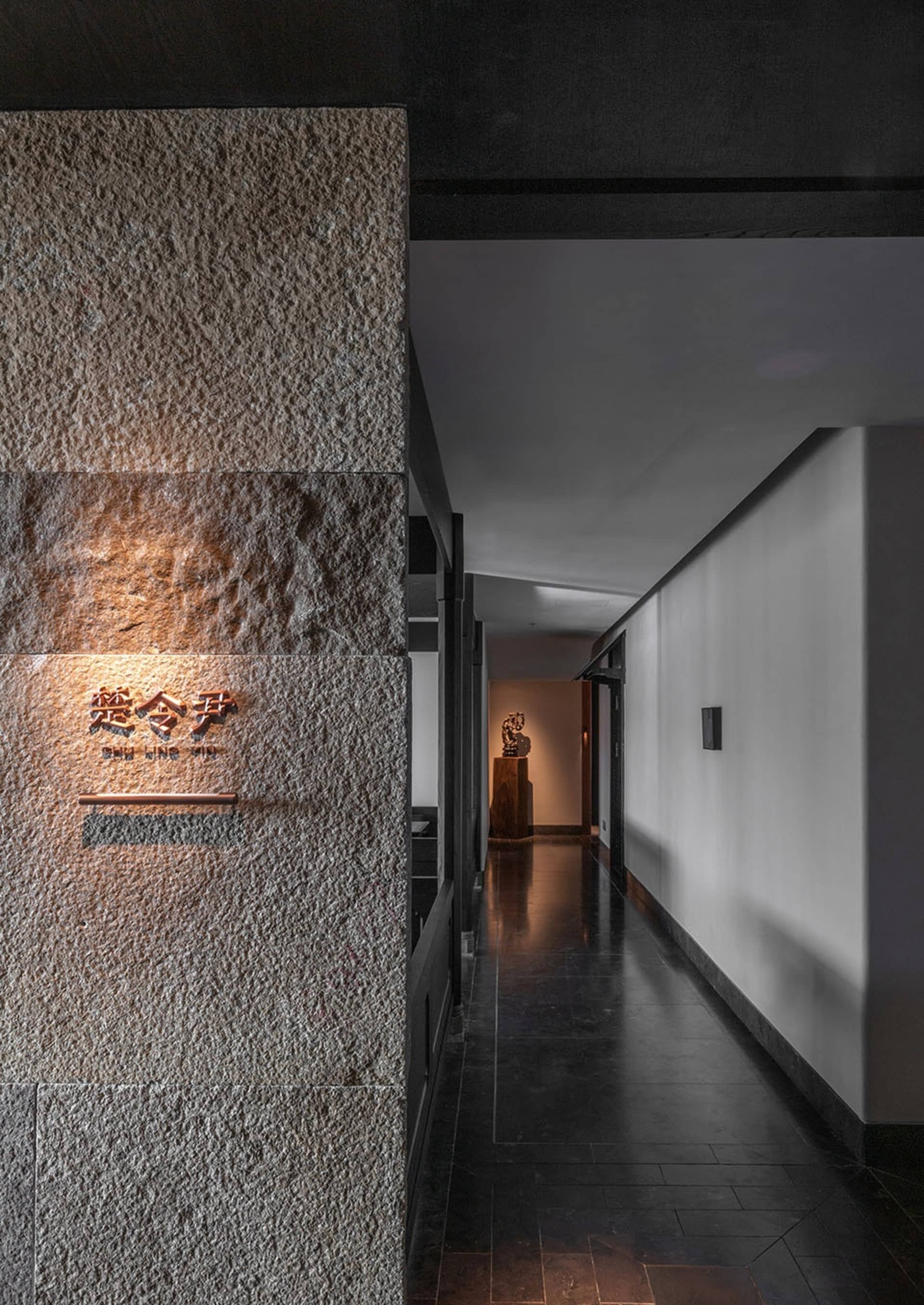 A dimly lit hallway with a stone wall and a wooden door, featuring two statues and a mysterious atmosphere