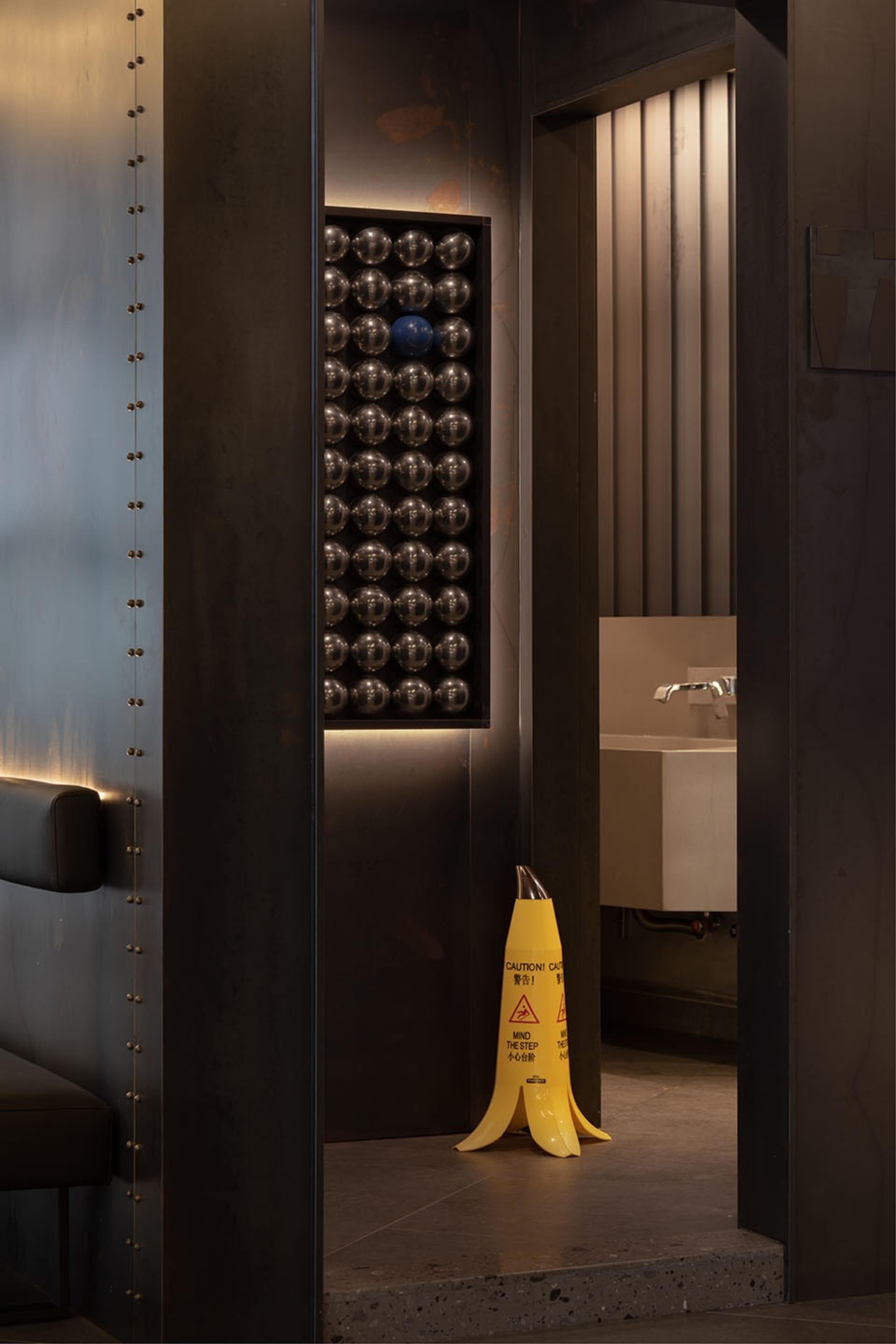 Industrial bathroom with metal walls, a yellow caution cone, and balls hanging from the ceiling, conveying a functional and utilitarian atmosphere