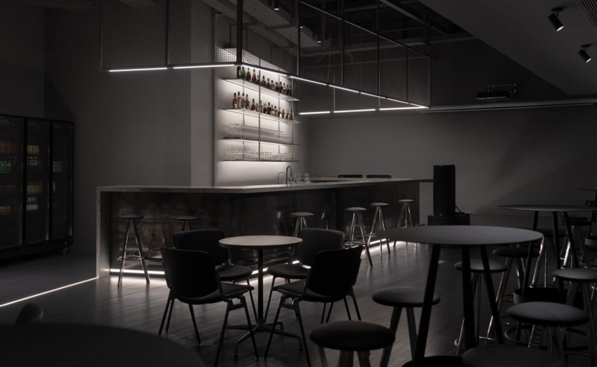 A dark and intimate bar area with a long wooden countertop and multiple chairs, surrounded by bottles and a well-stocked display