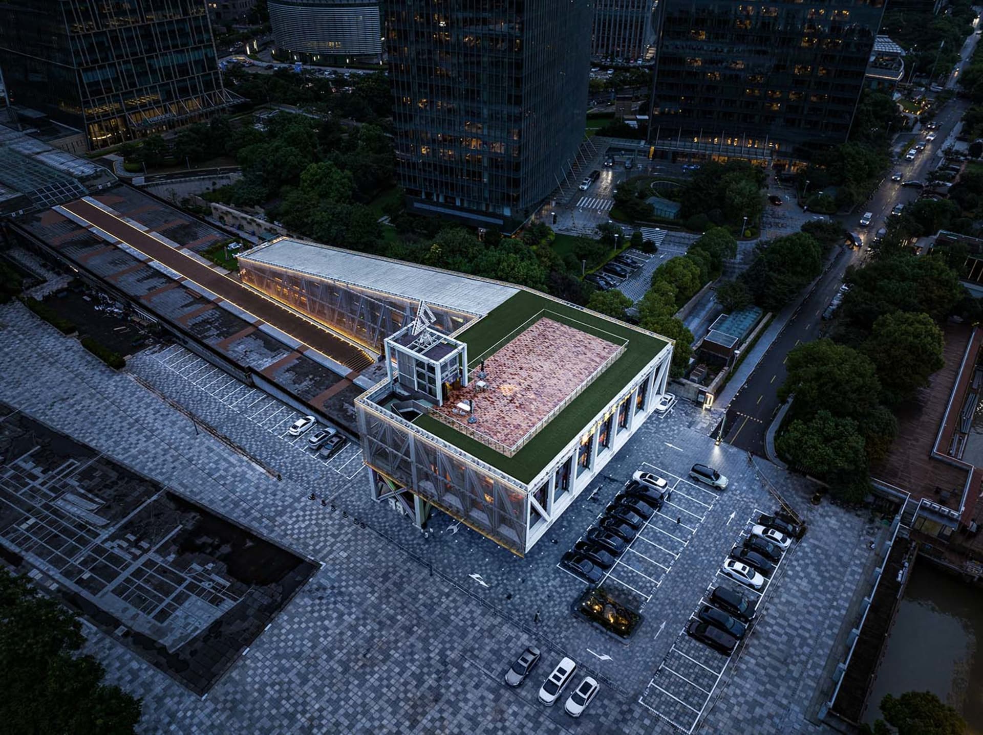 A modern building with a white exterior and a green roof, set against an urban backdrop with parked cars and a contemporary atmosphere