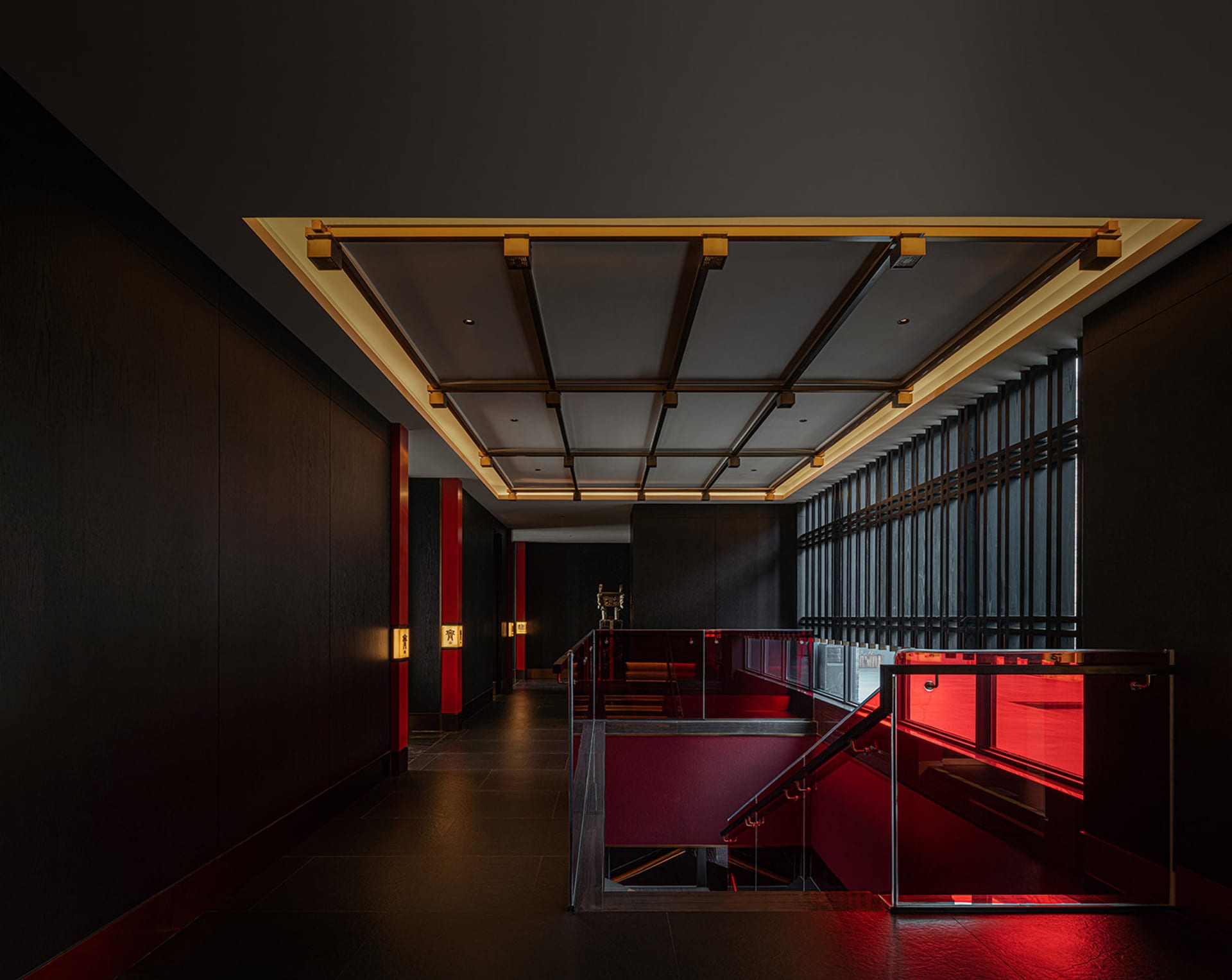 A modern interior space with a glass staircase, black walls, and red accents, featuring a bench at the base of the stairs
