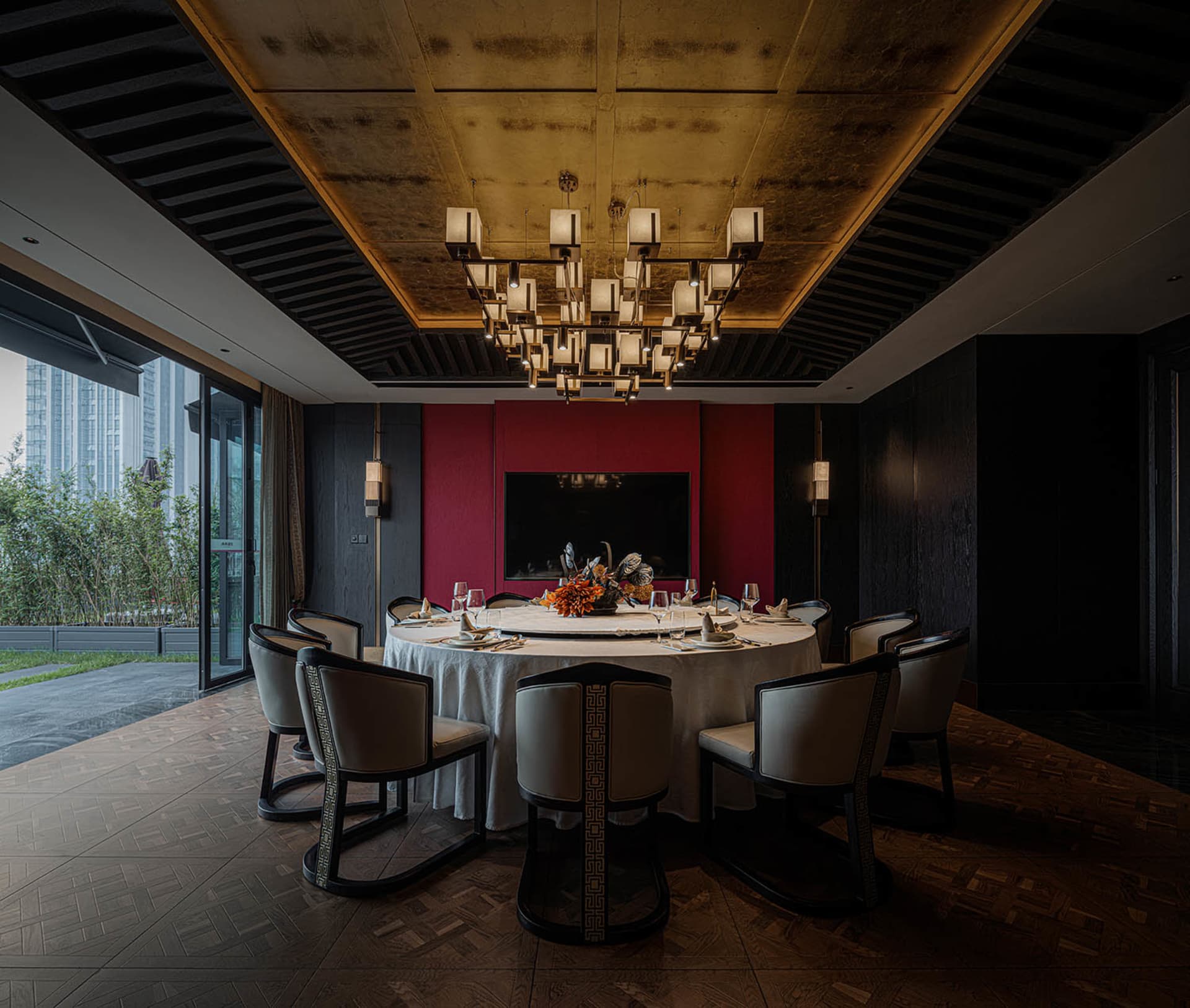 A modern dining area with a round table, red walls, gold accents, and various table settings, creating a luxurious and inviting atmosphere