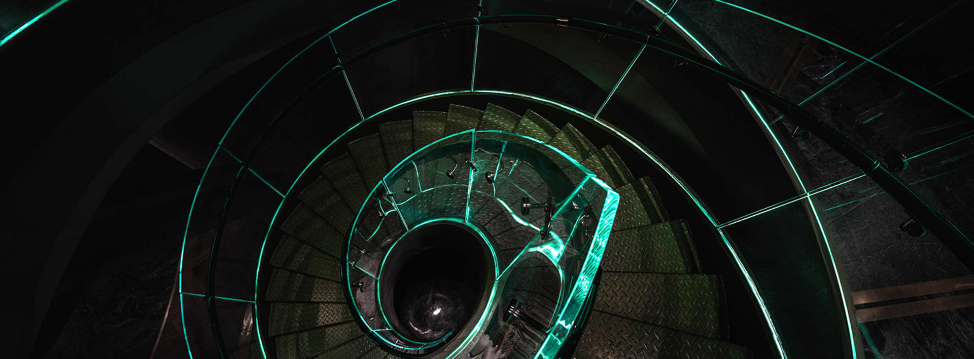 A futuristic spiral staircase with green lighting, made of metal, in a modern building