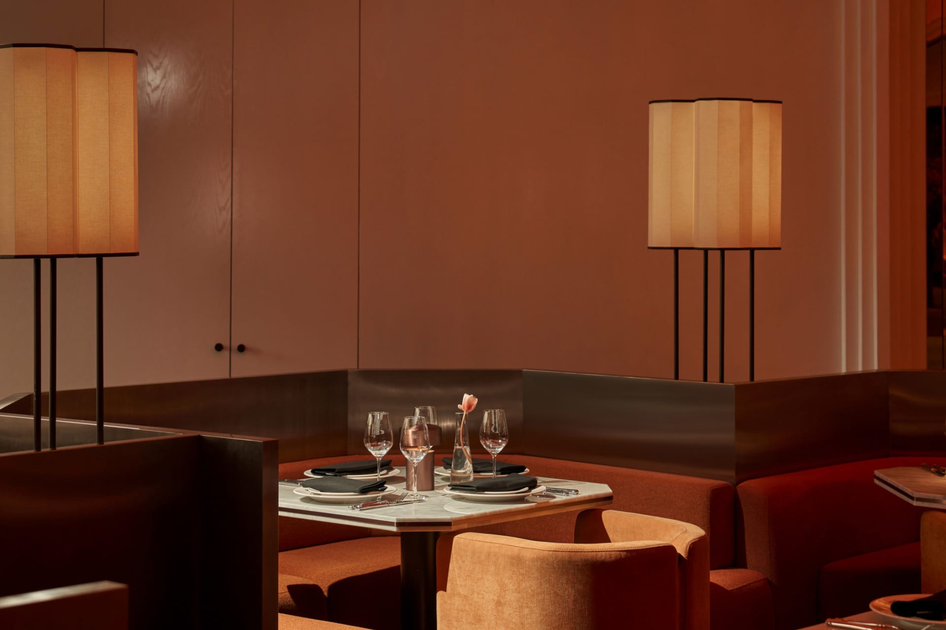 Dining area with a table, chairs, wine glasses, and a vase, surrounded by warm red-hued walls