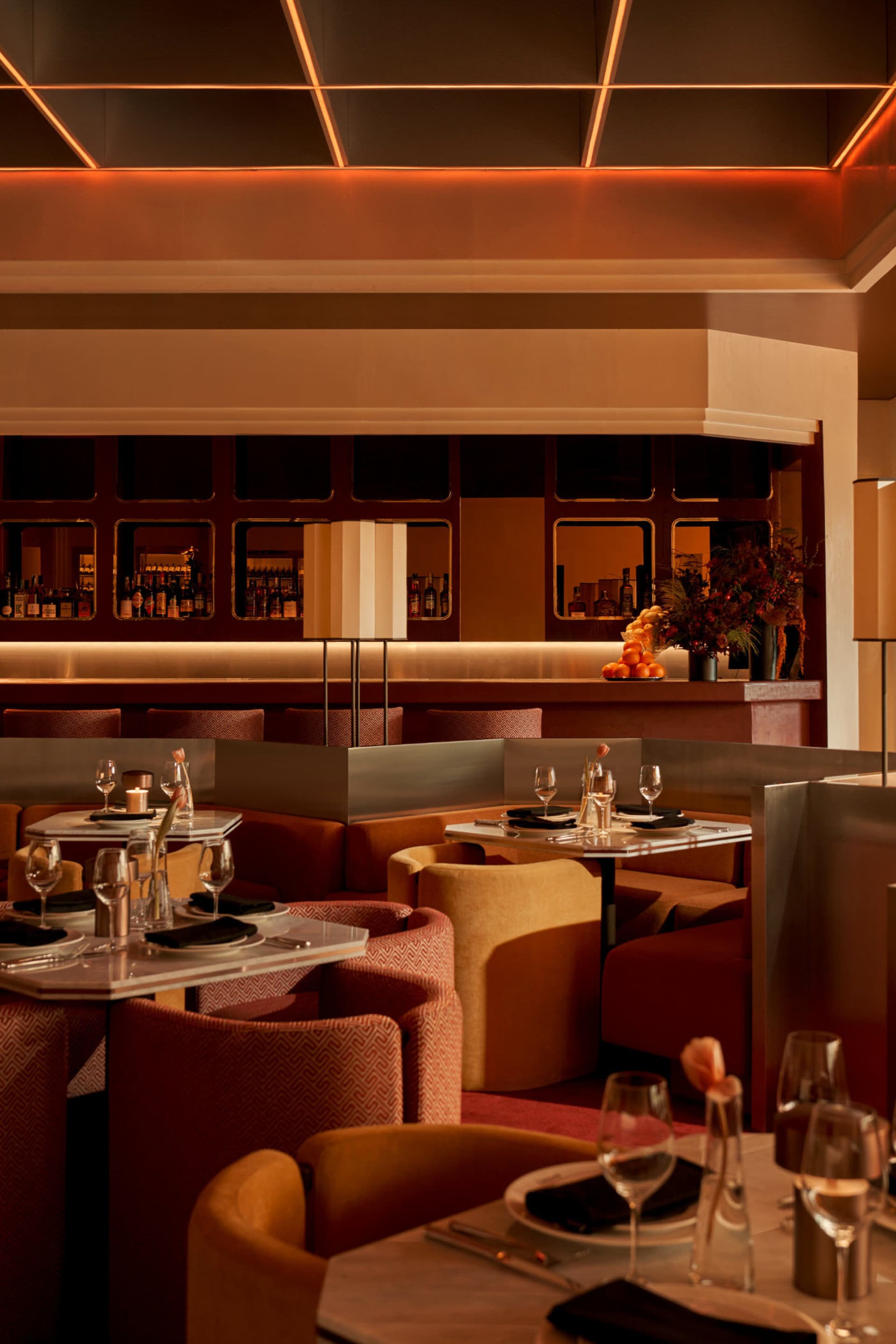 A cozy restaurant with a long dining table and chairs, wine glasses, and cups, surrounded by couches in the background