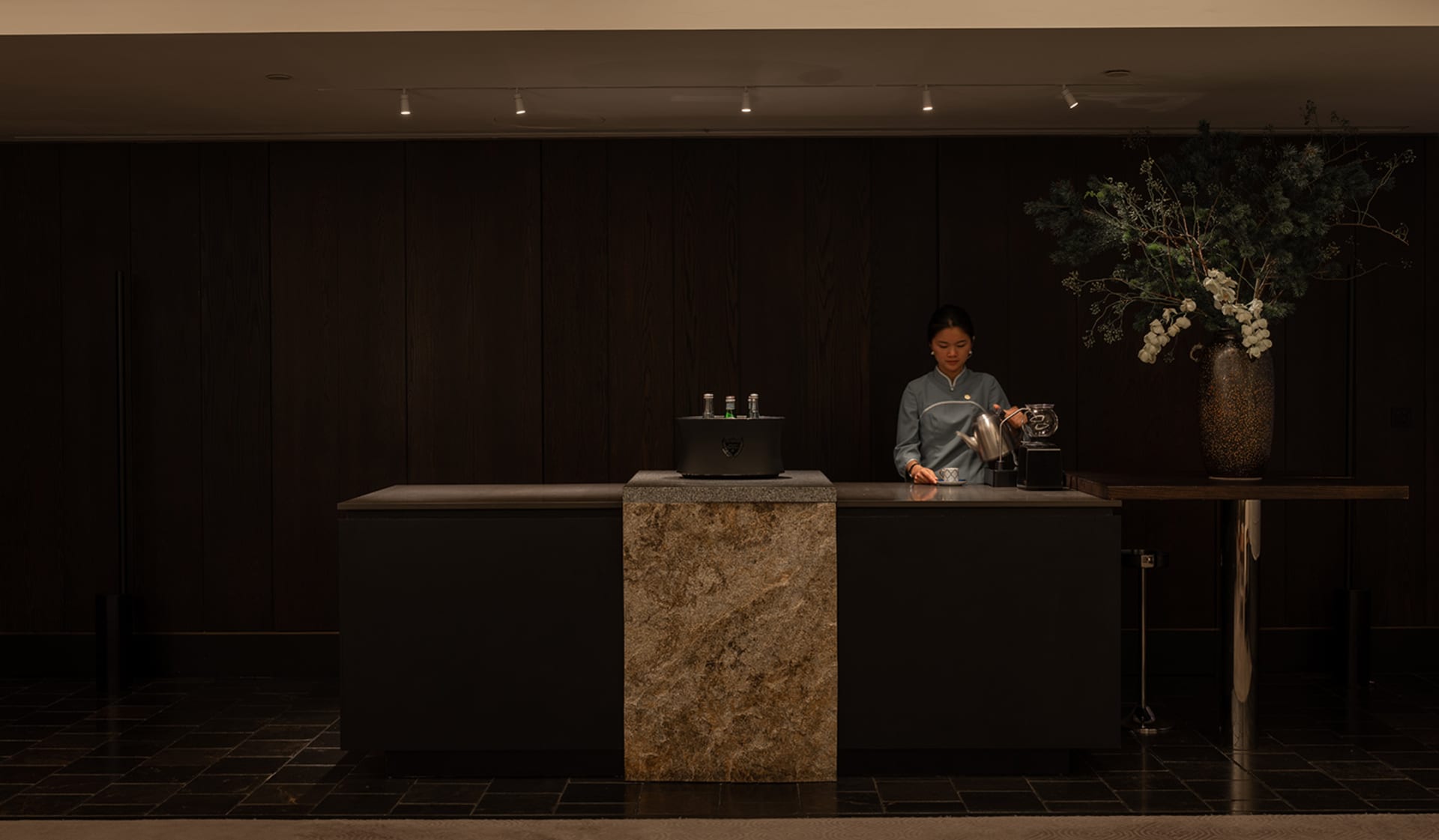 A casual cafe interior with a wooden counter, a coffee maker, and a woman standing behind it