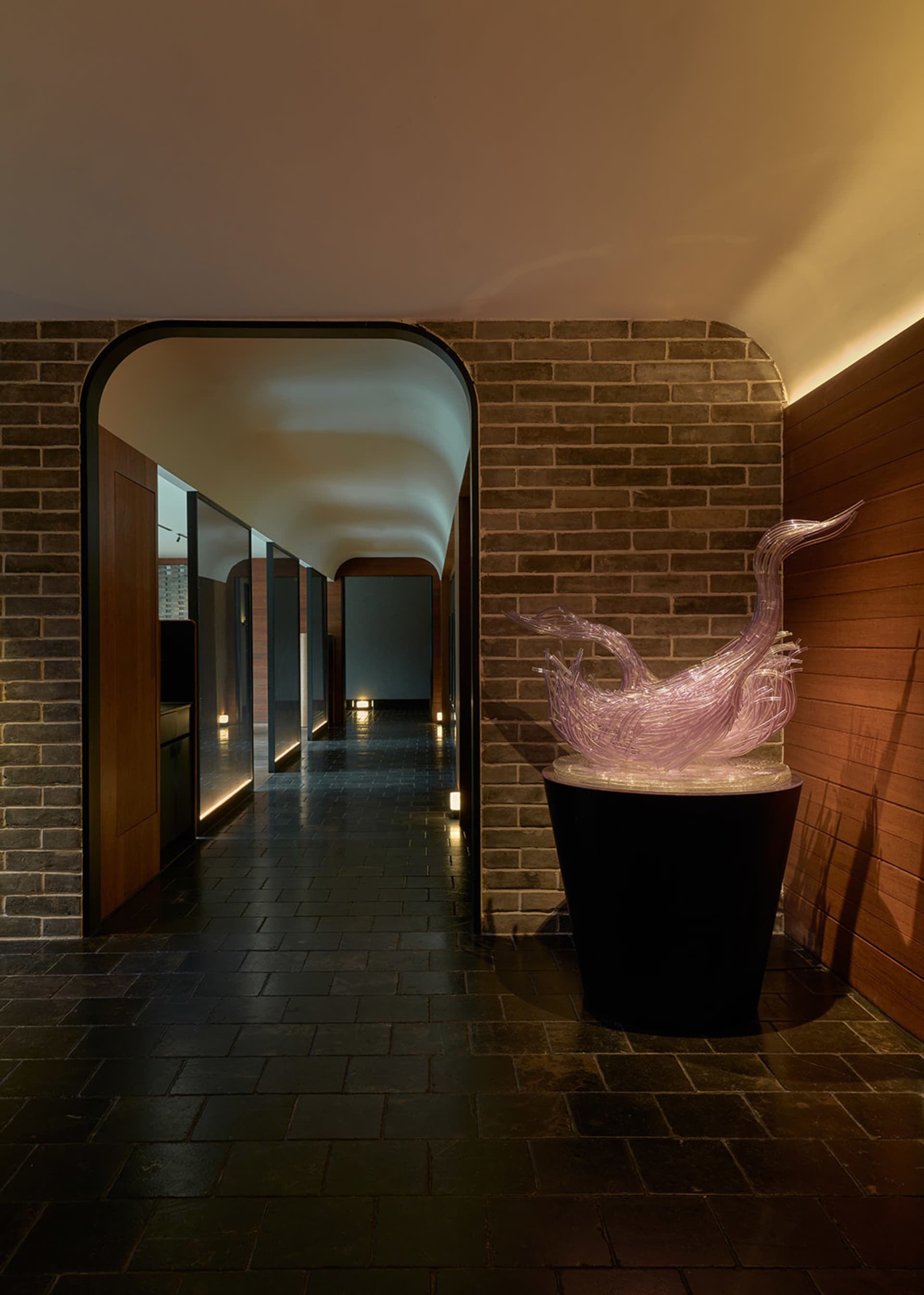 A dimly lit hallway with brick walls, featuring three potted plants and two doors on either side