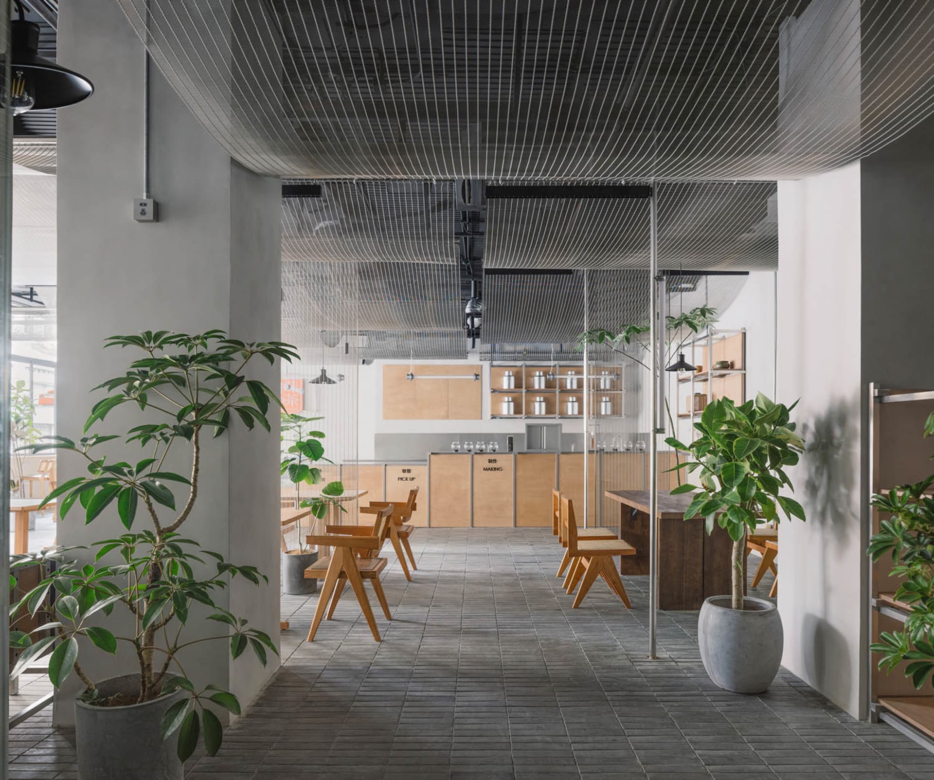 Cozy cafe interior with wooden floors, tables, chairs, and potted plants, featuring a tiled pattern on the walls and well-lit atmosphere