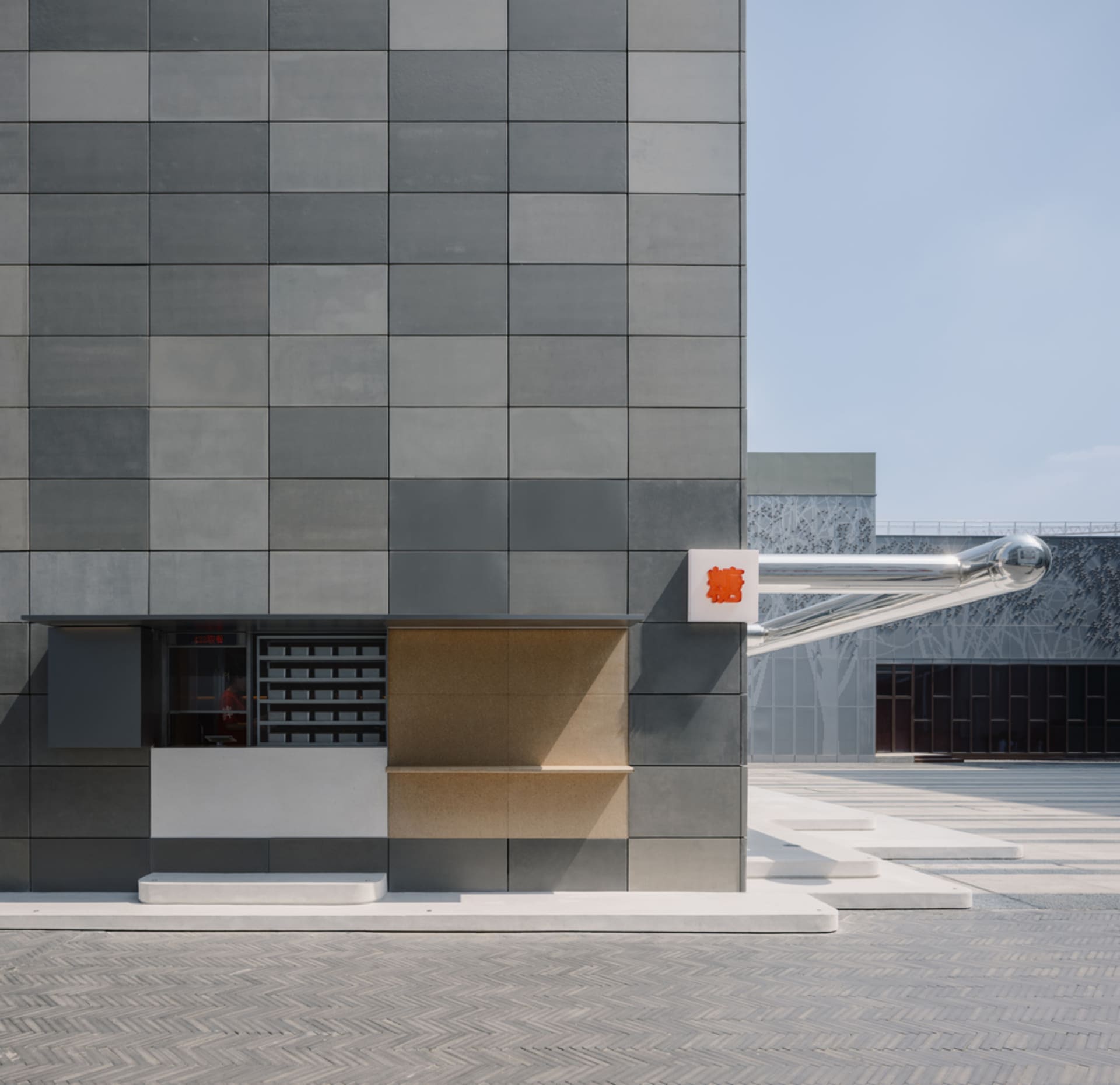 Exterior view of a modern building with a large gray wall featuring unique design elements and two signs, set against a clear blue sky