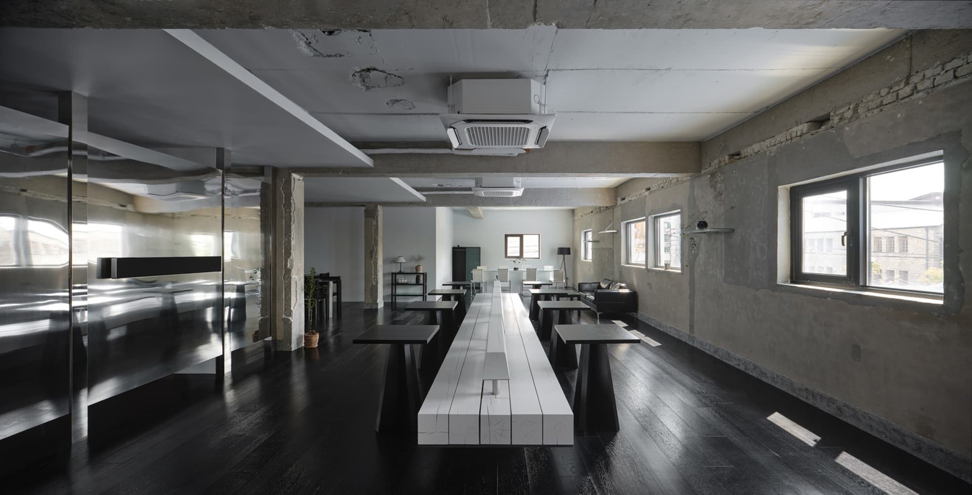 A clean and well-organized dining area with a long white table, multiple chairs, and potted plants, set in a commercial building