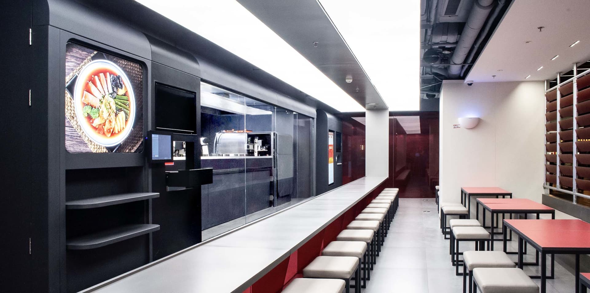 Industrial kitchen with modern black cabinets, red accents, and a long counter with chairs and two TVs mounted on the wall
