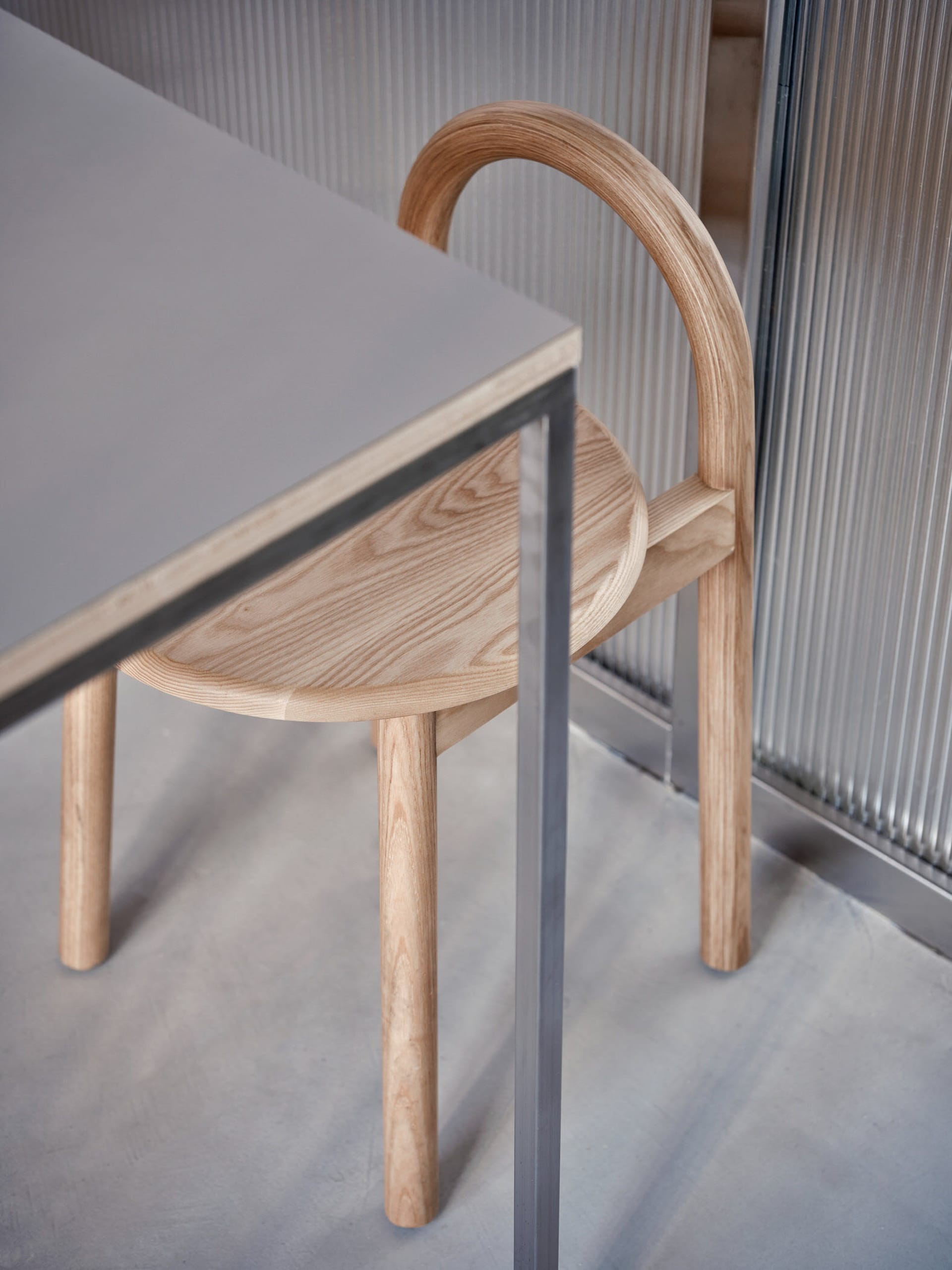 A cozy indoor space with a wooden chair on a grey carpet in front of a table, featuring a modern metal-framed chair