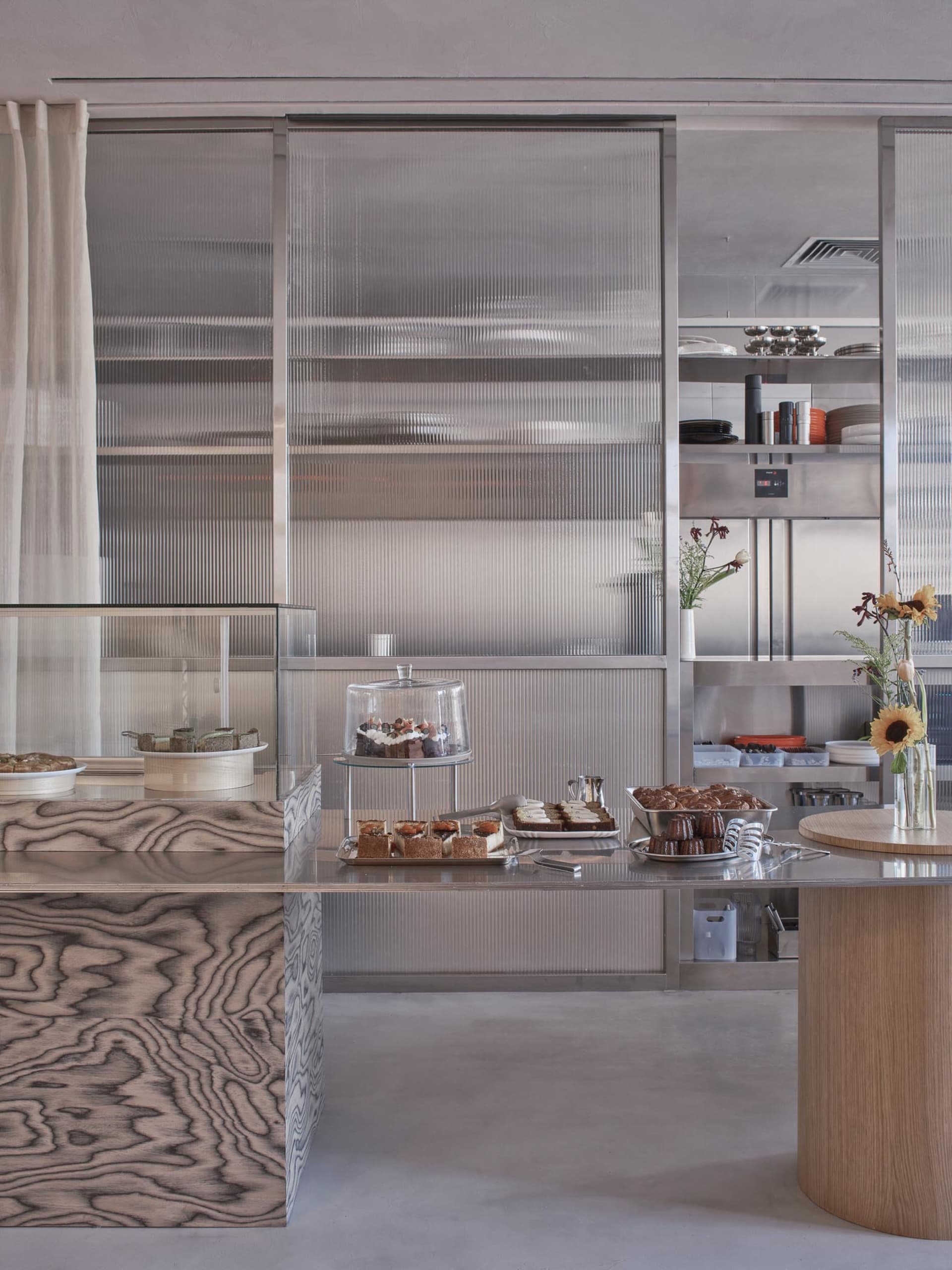 Modern restaurant kitchen with stainless steel appliances and surfaces, a counter with displayed food items, and a contemporary atmosphere