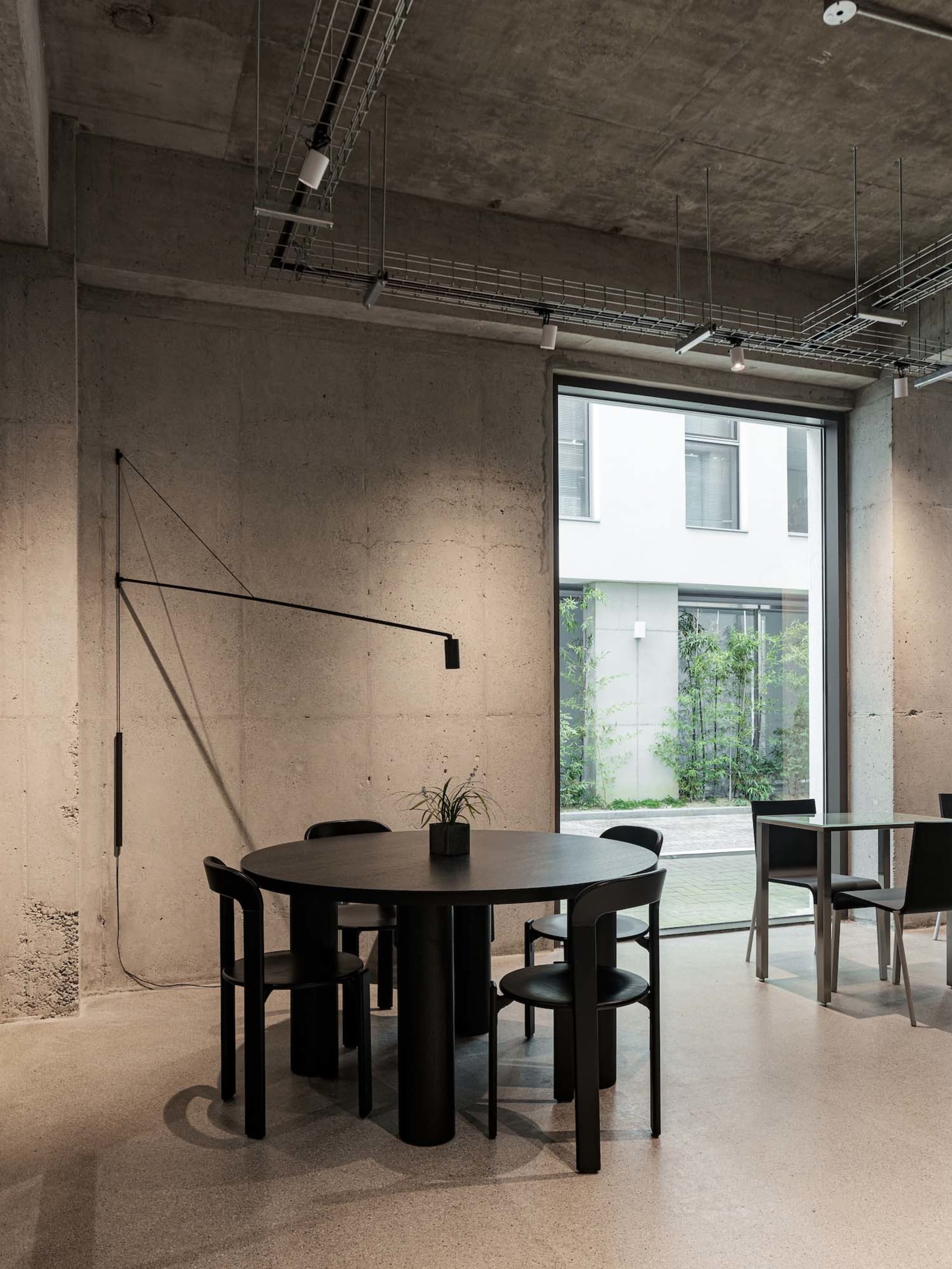 A minimalist dining space with a black table, chairs, and potted plants, surrounded by clean lines and neutral tones, in a well-lit atmosphere