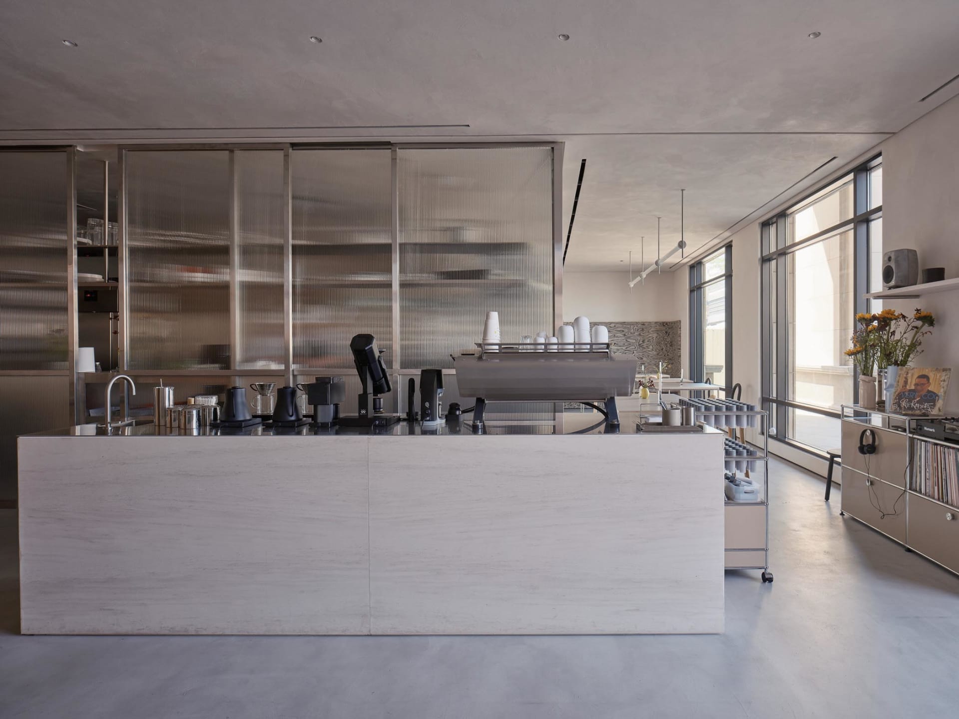 Industrial kitchen with a counter featuring cups, bottles, coffee pots, and bowls, suggesting a functional workspace