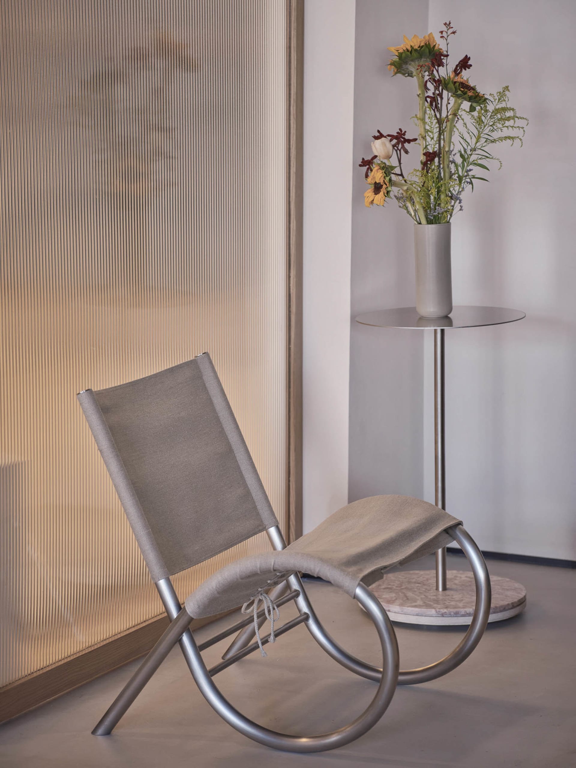 A modern room with a gray metal chair on a hardwood floor, surrounded by vases and potted plants