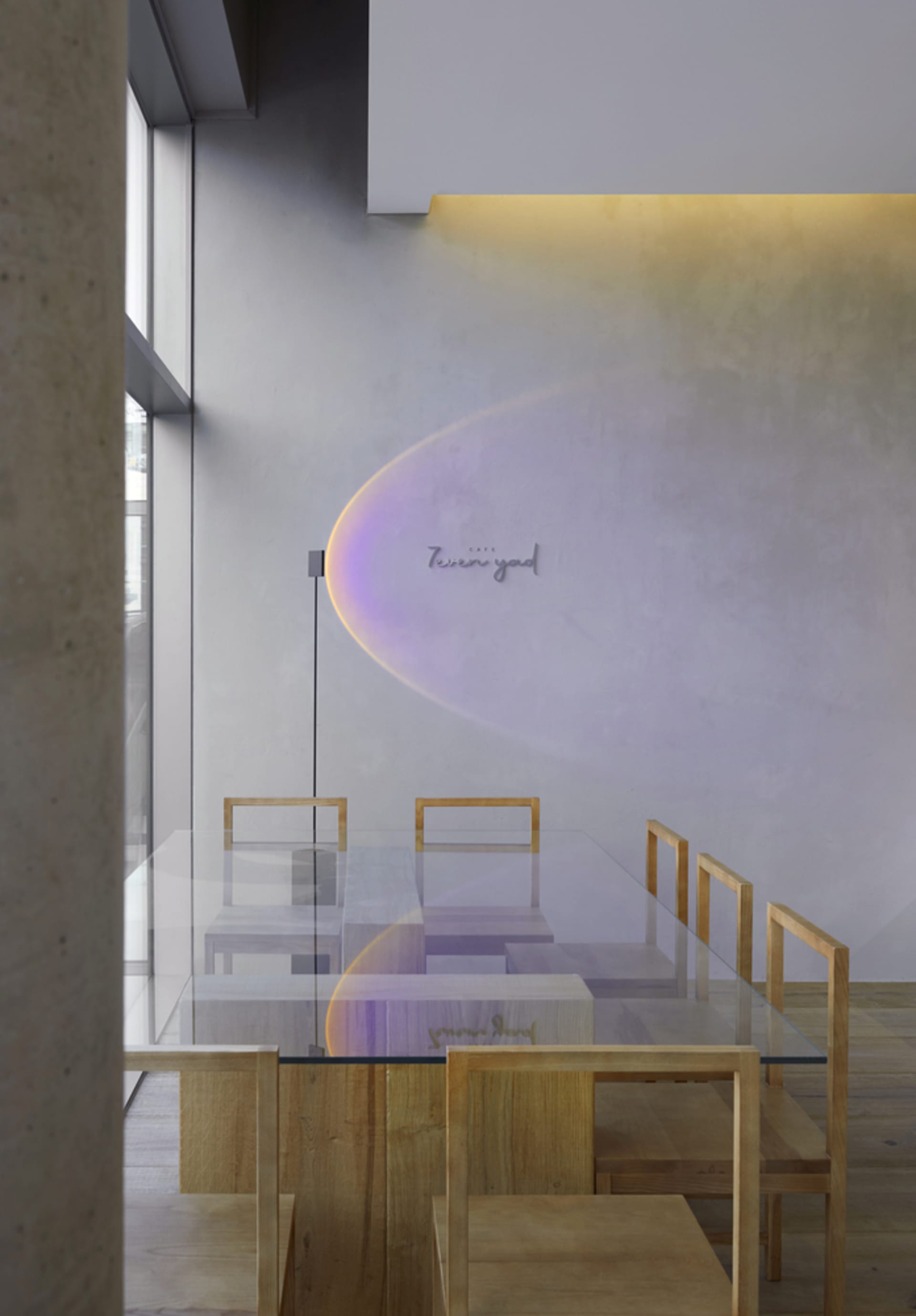 A modern restaurant interior with a large glass dining table surrounded by wooden chairs, bathed in bright natural light