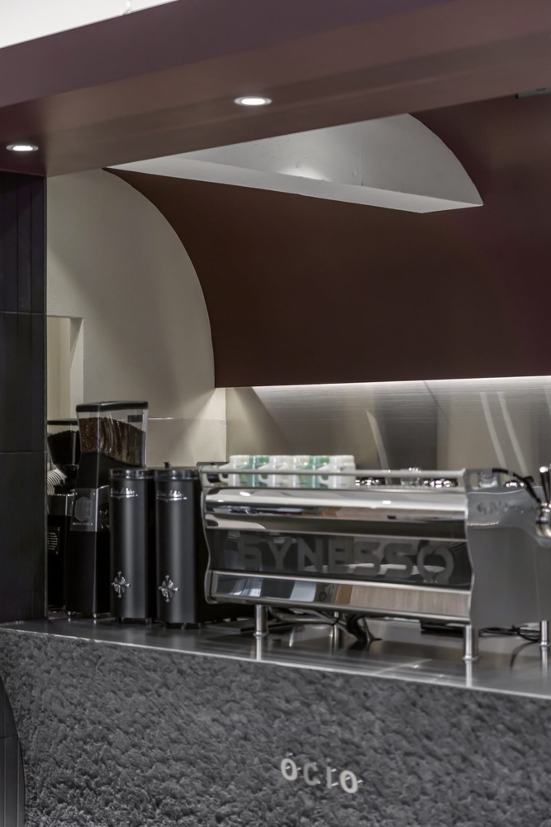 Industrial kitchen with a silver coffee machine, cups, and bottles on a countertop, suggesting a professional food preparation environment
