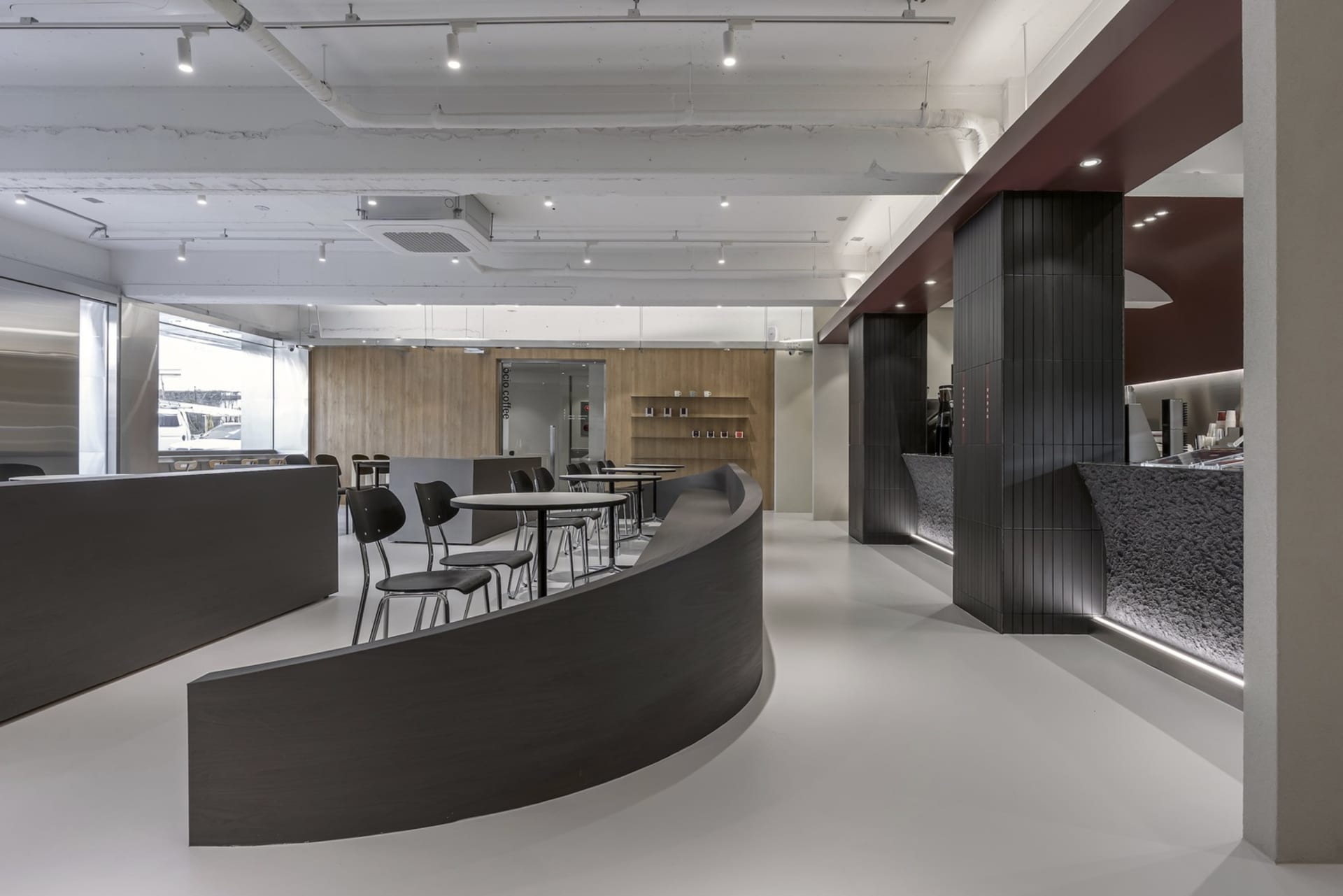 Open restaurant interior with curved design, wood, and metal elements, featuring chairs and dining tables in a modern and inviting atmosphere