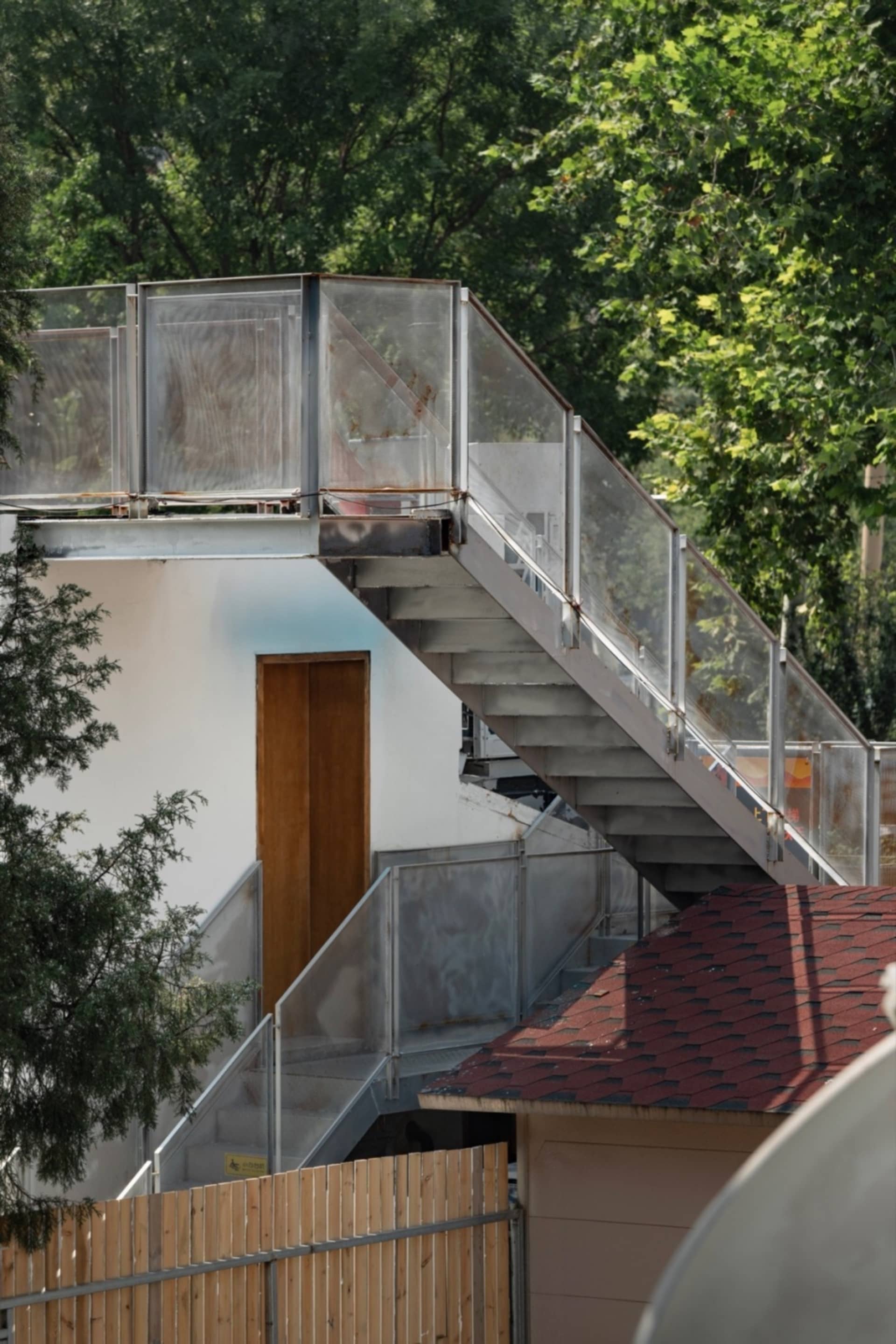 A modern house with a metal staircase leading to a doorway on the second floor, with an open doorway revealing the interior and a calm, inviting atmosphere