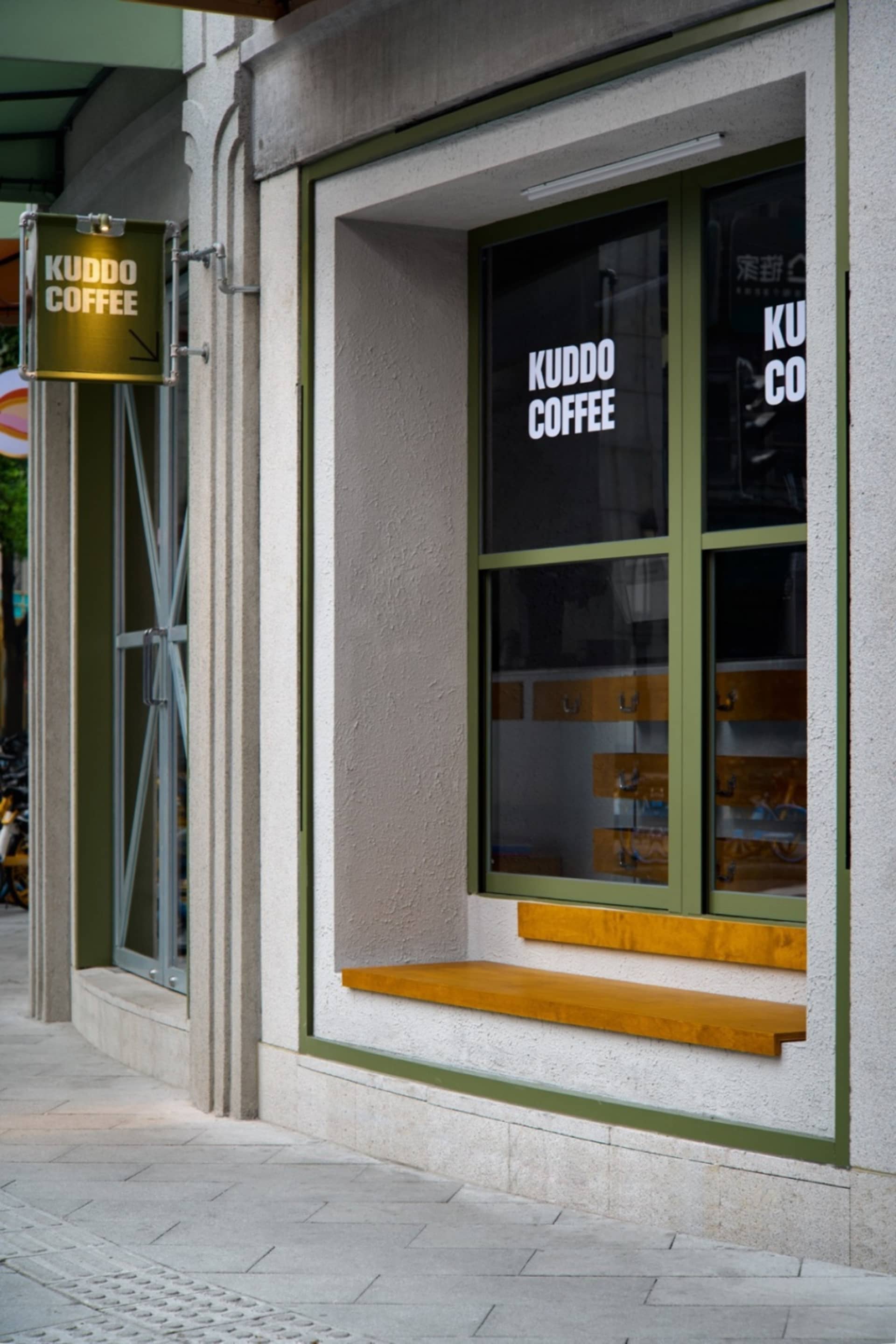 Exterior view of a coffee shop with a wooden bench and green frame, surrounded by bicycles and inviting atmosphere
