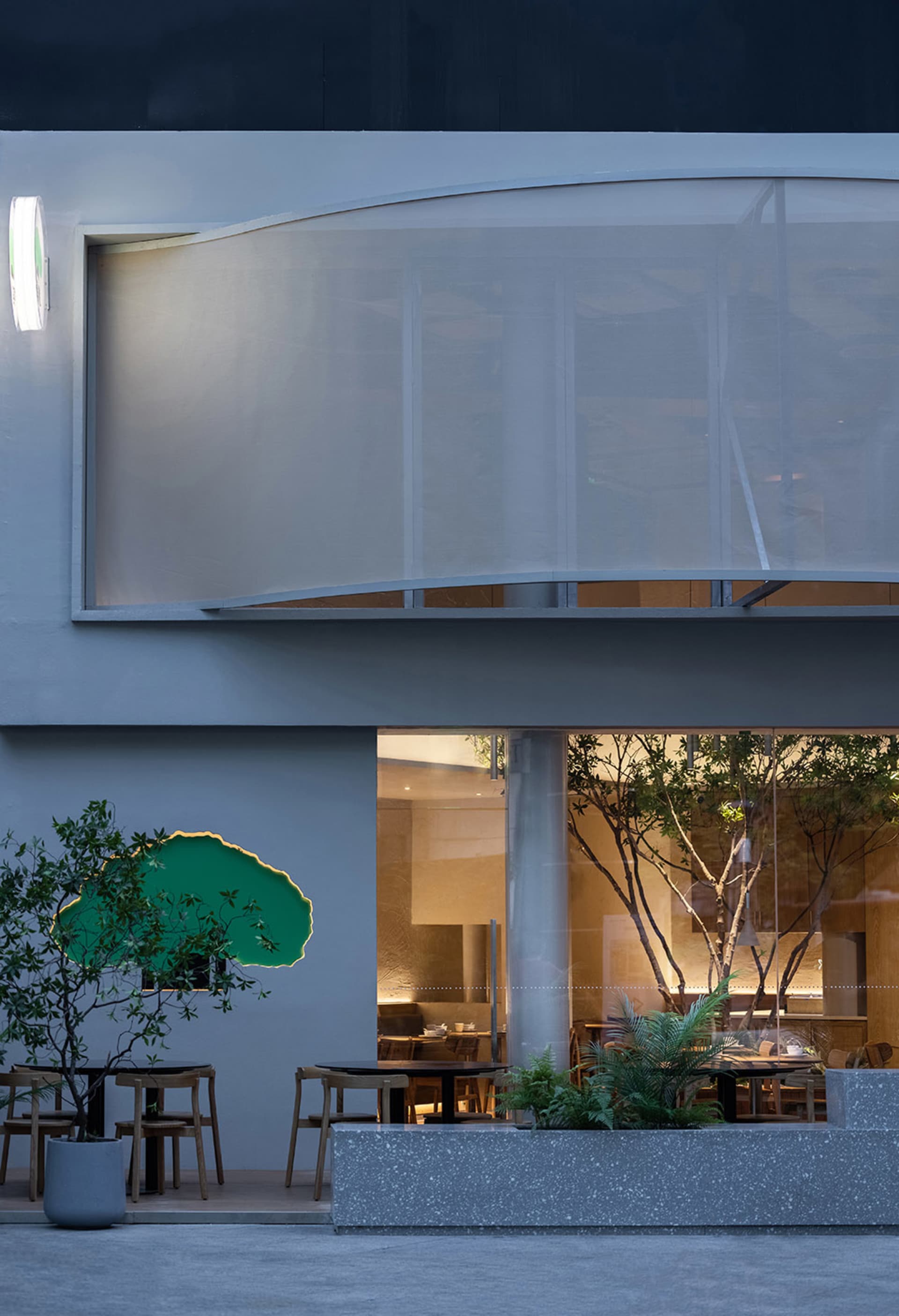 Modern restaurant interior with natural light, wood, and glass elements, multiple dining tables and chairs, and a warm atmosphere