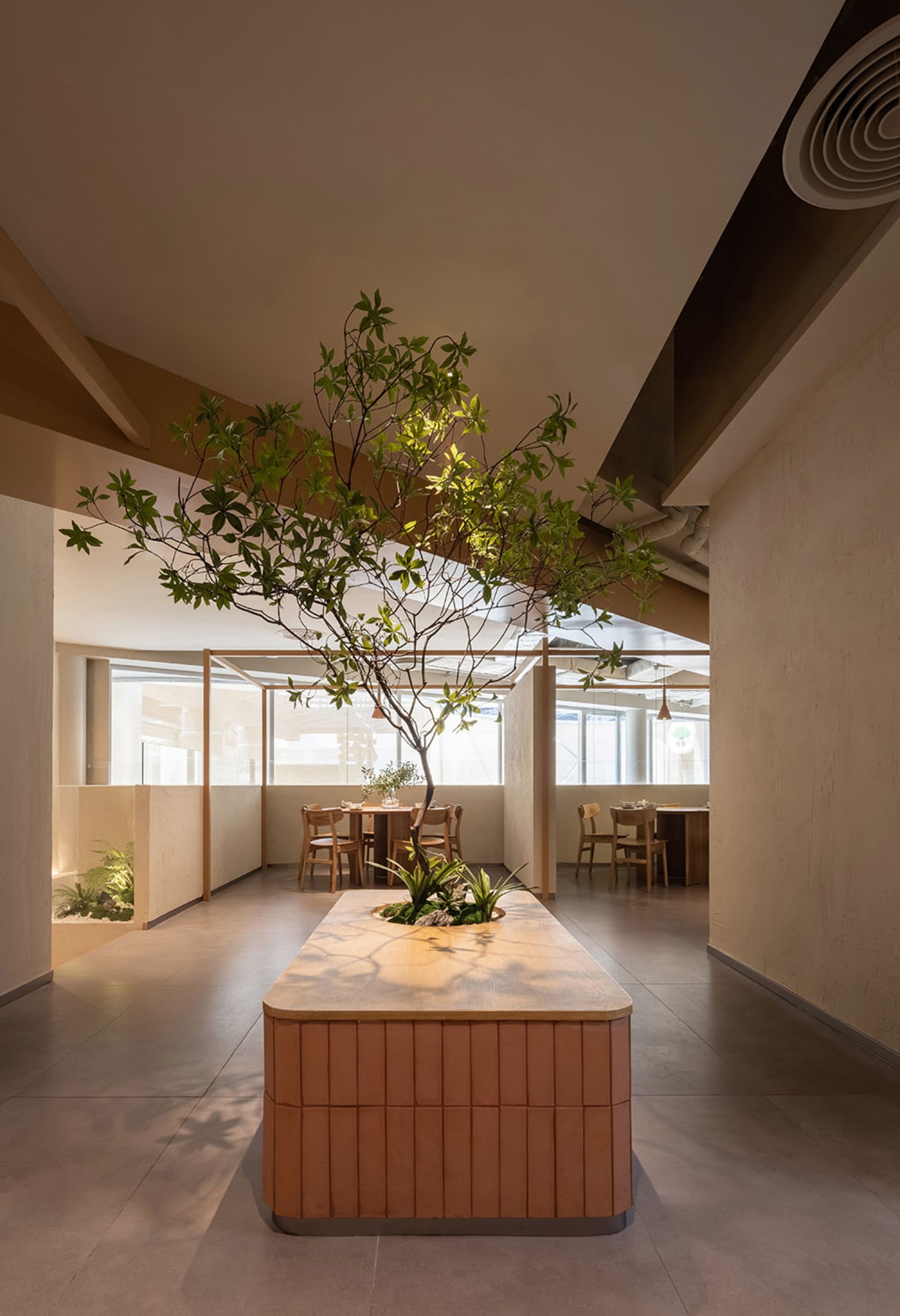 A modern restaurant interior with a large dining table, potted plants, and concrete walls, creating a cozy atmosphere
