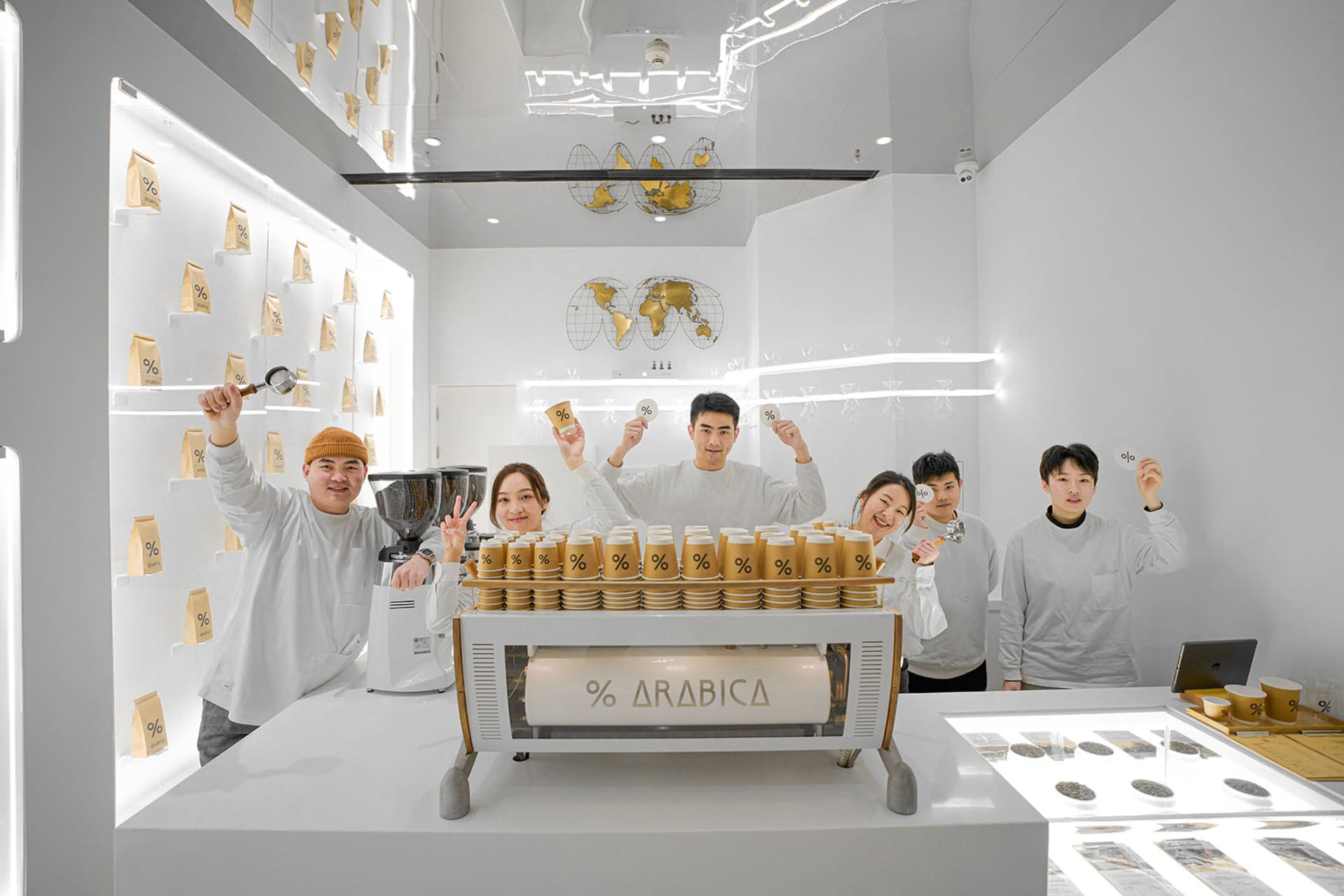 A group of people posing in front of an Arabica coffee machine with various canisters on display, creating a friendly and inviting atmosphere