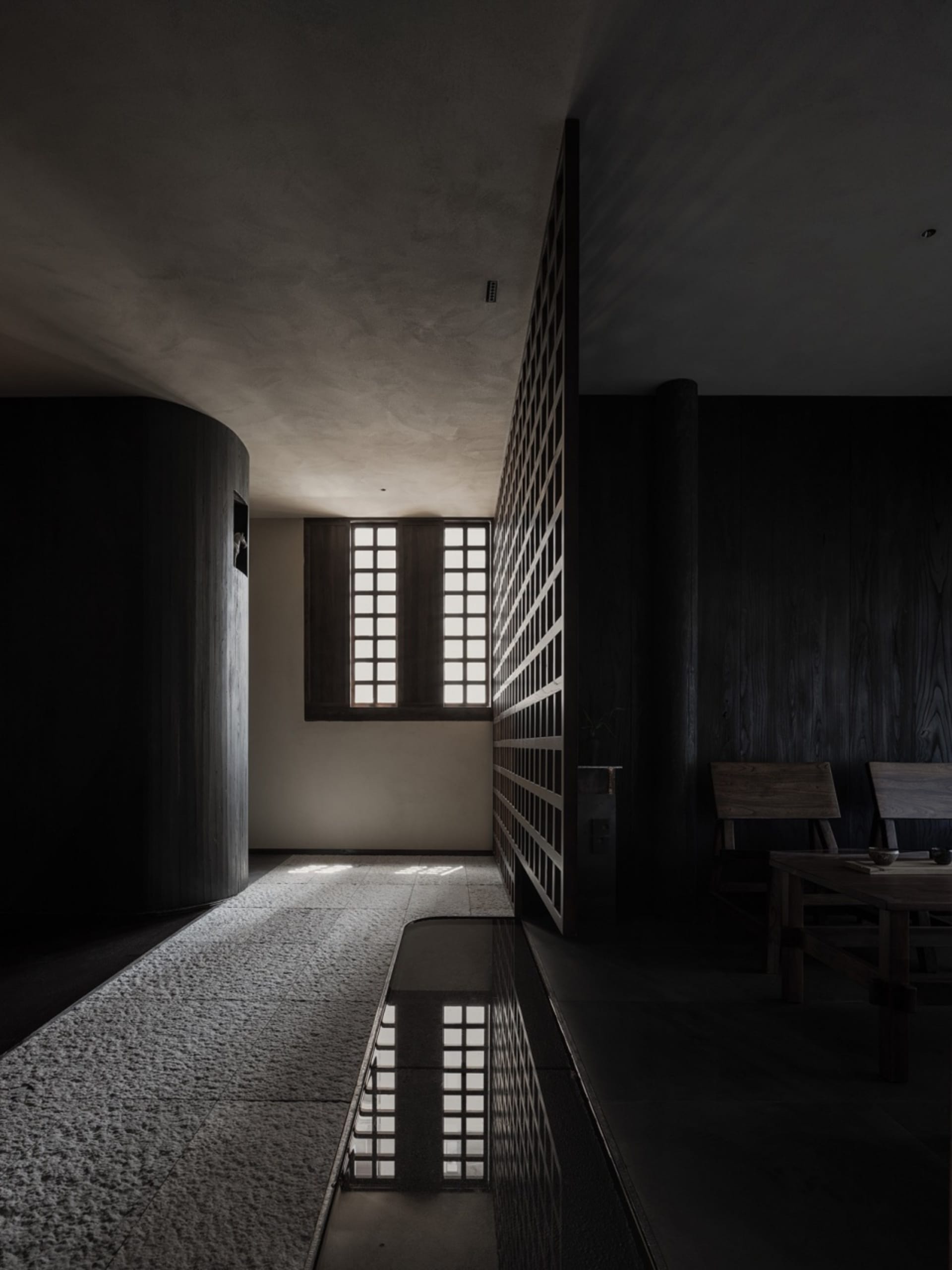 Dimly lit hallway with a wooden door, two chairs, and a dining table, creating a cozy and mysterious atmosphere