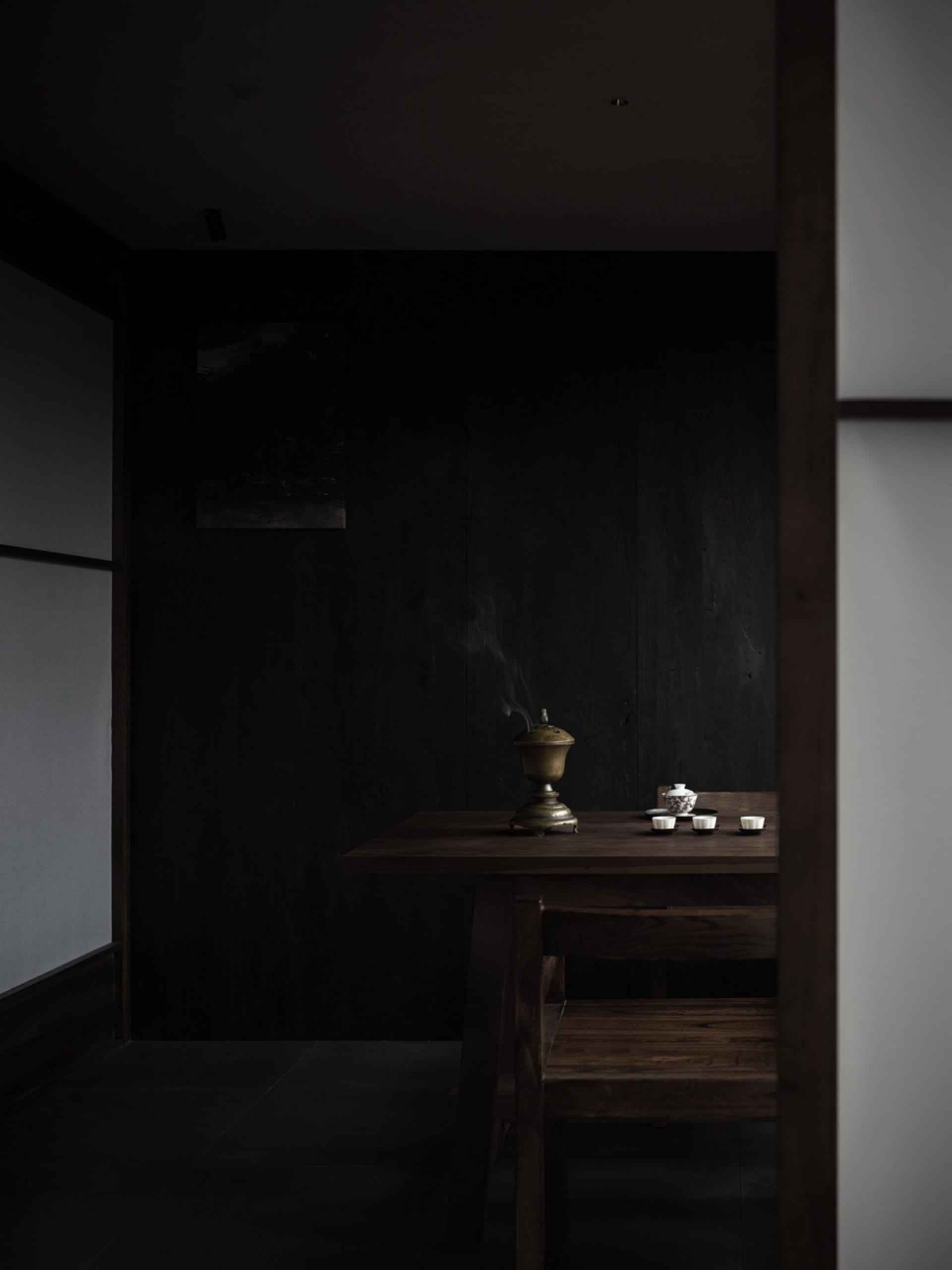A dimly lit dining room with a dark wooden table, two bowls of food, cups, and a vase, creating a cozy and intimate atmosphere