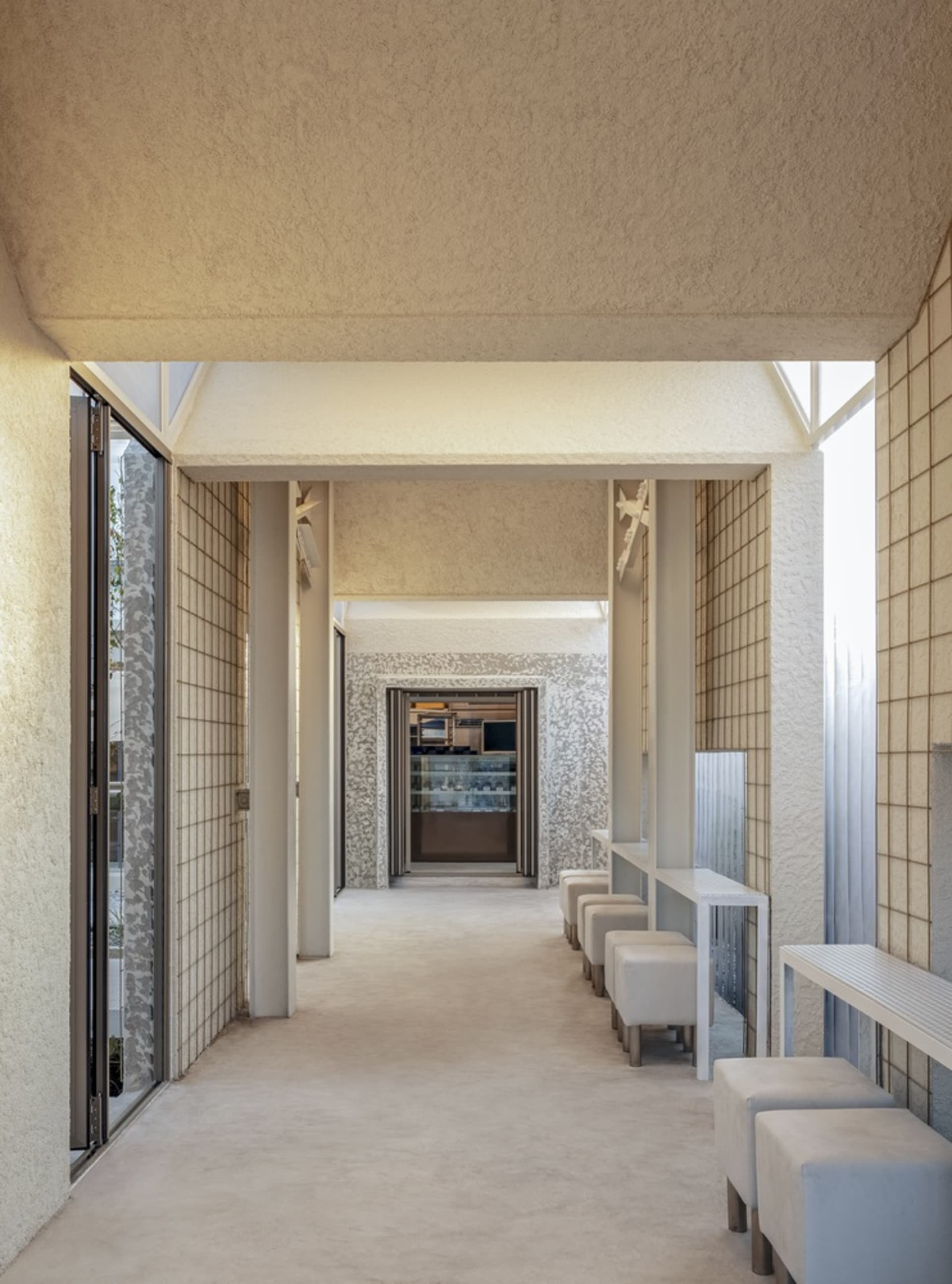 A clean and well-lit hallway with white walls and floors, featuring several chairs placed throughout the space