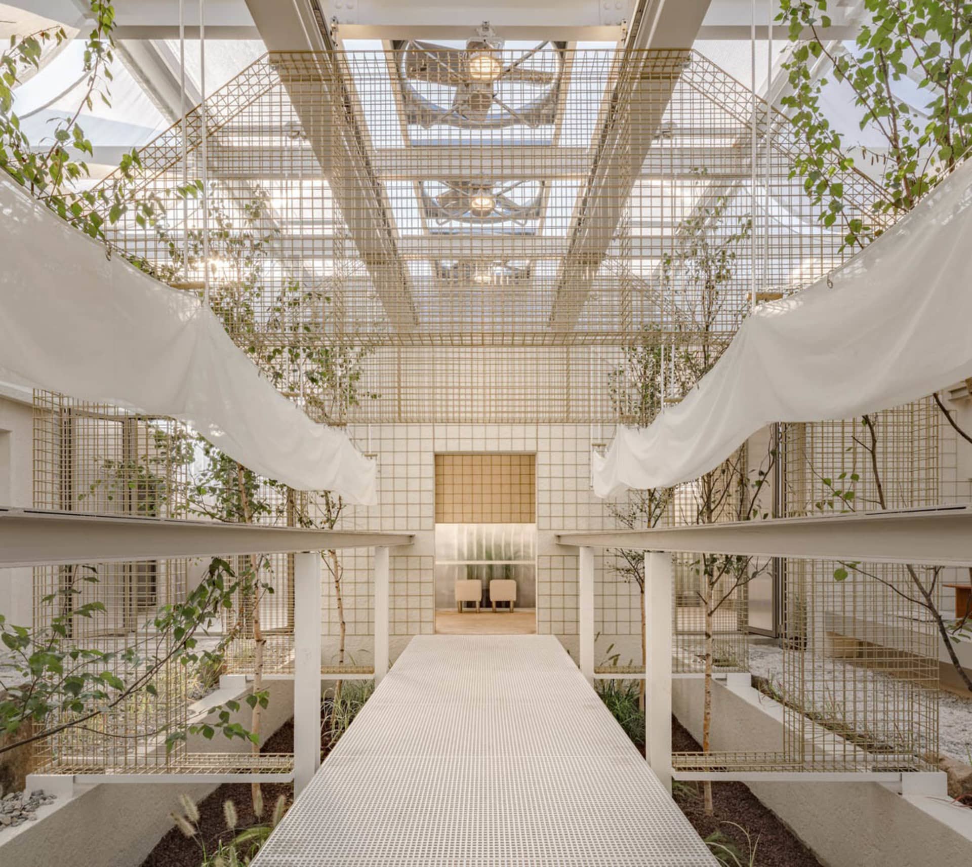 A modern indoor space with a white staircase surrounded by plants and trees, featuring potted plants on the ground and hanging from the ceiling