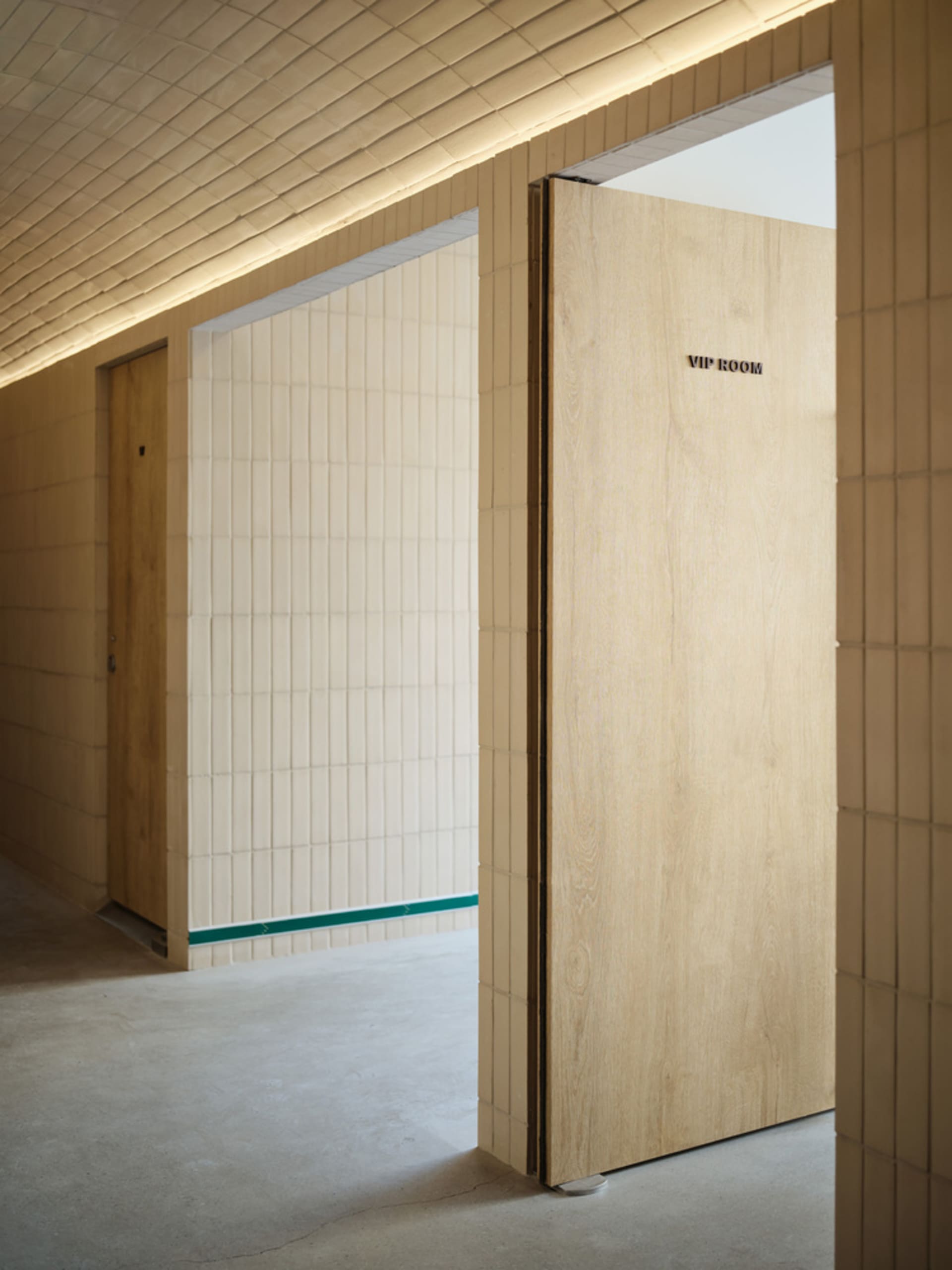A bright and inviting hallway with open doors to a small room, featuring ceramic tile walls and natural light