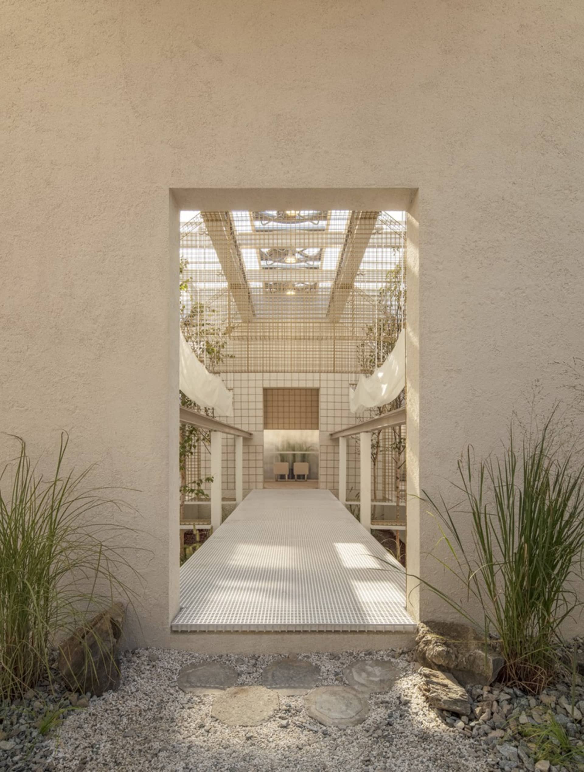 A calm hallway with a white tile floor and potted plants adding greenery and depth to the space