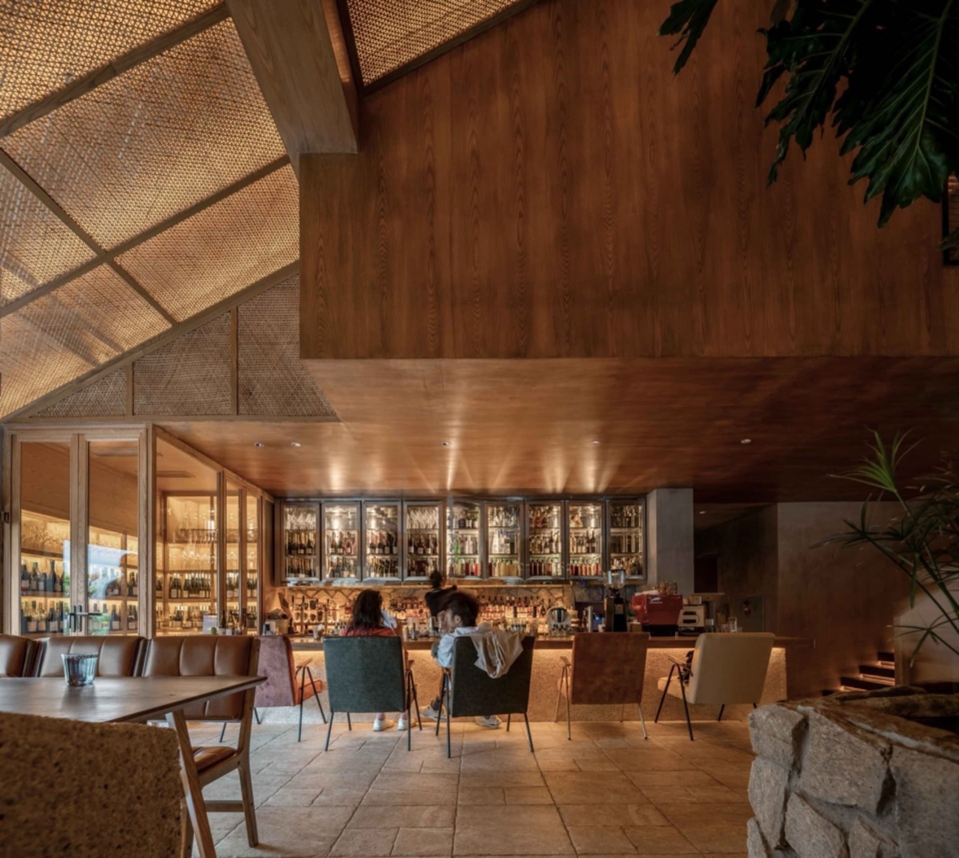 A social bar area with a dining table surrounded by chairs, bottles, and people enjoying a relaxed atmosphere