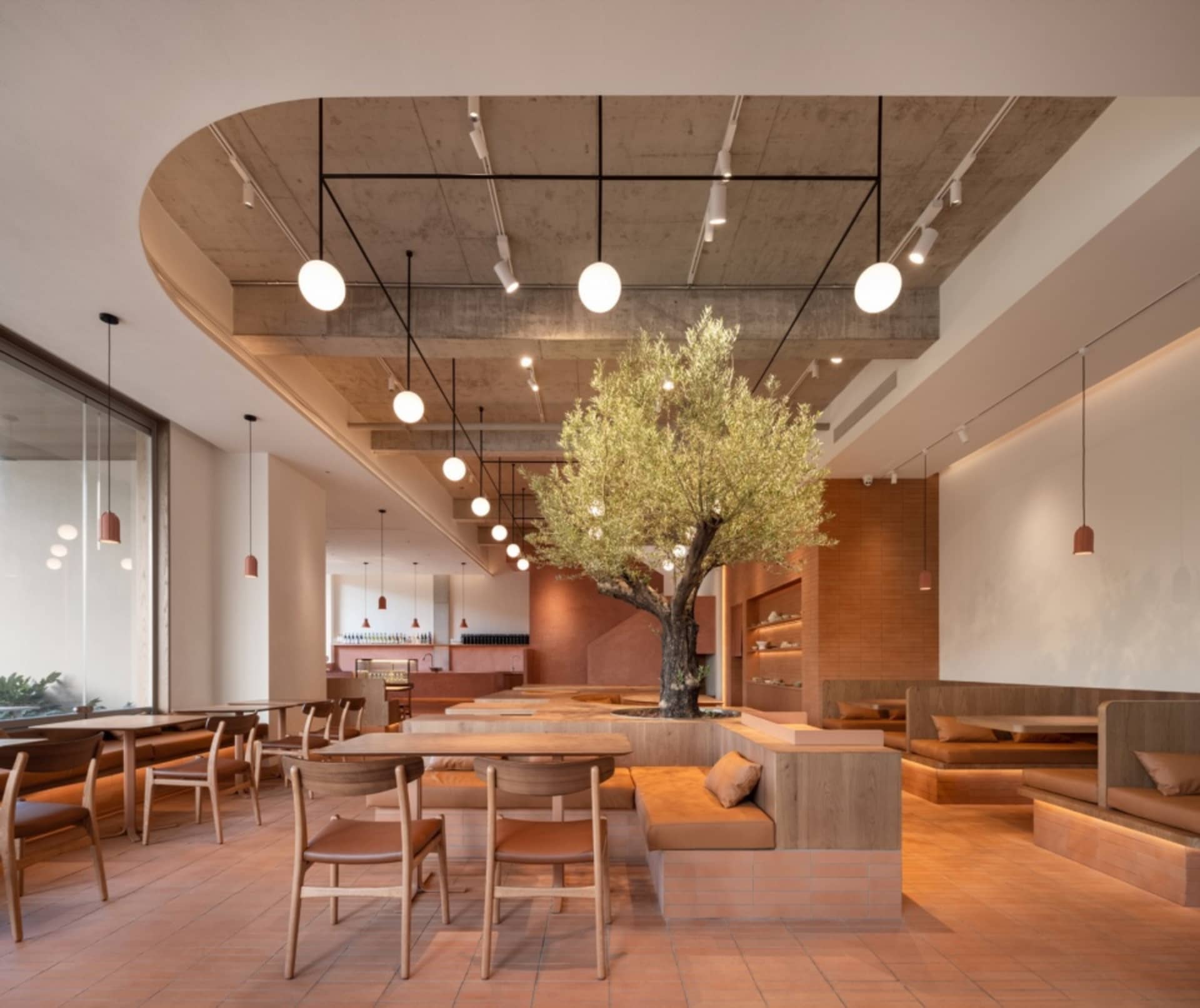 Open restaurant interior with multiple tables, benches, and a tree, featuring warm and inviting atmosphere
