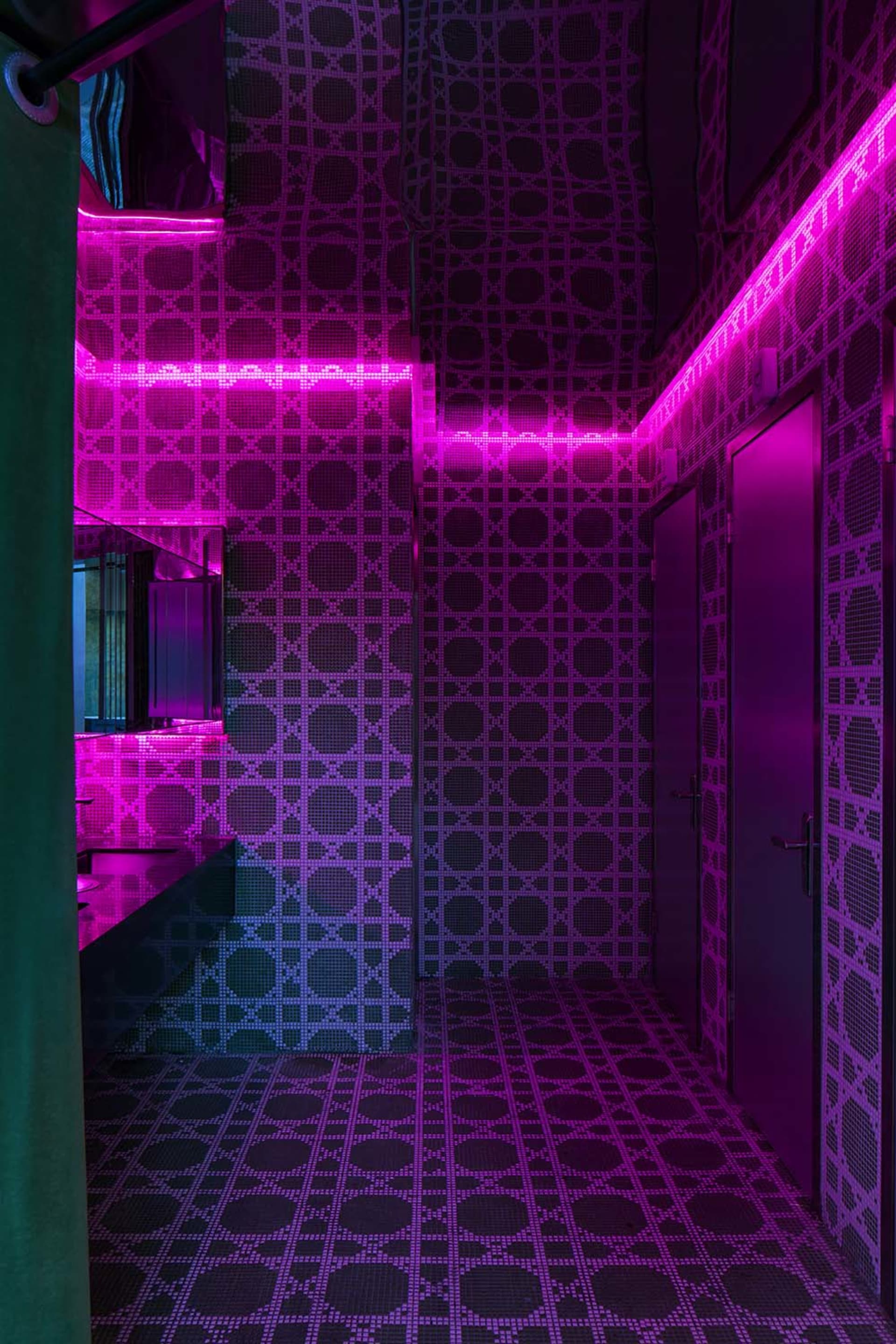 Bathroom with checkered patterned walls, pink and purple tiles, a sink, and a door