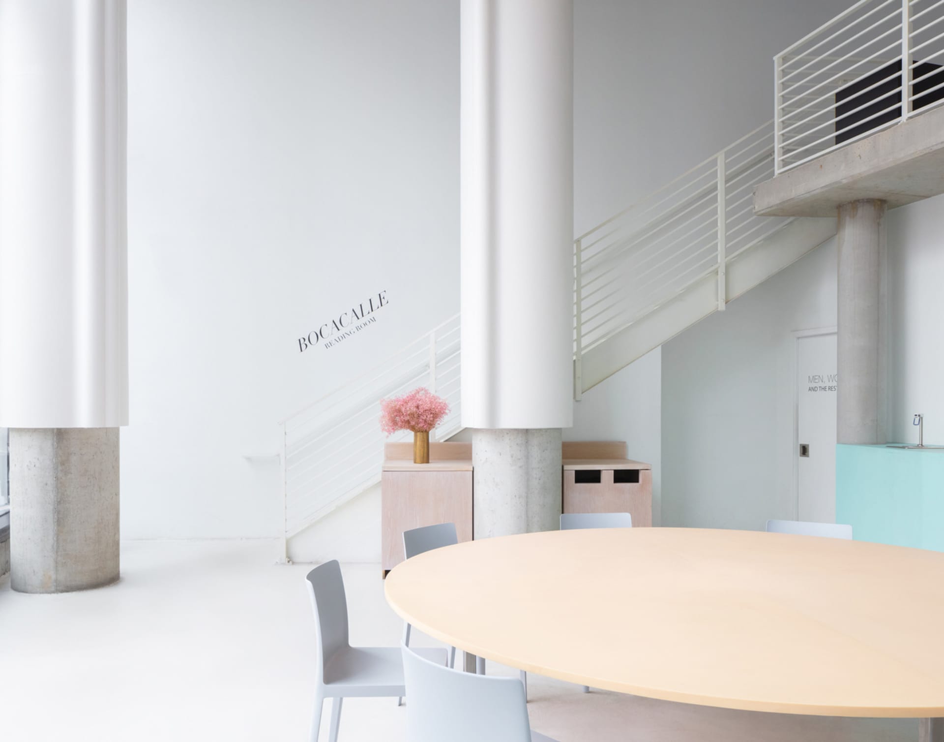 A calm and inviting lobby with a large wooden table and chairs, surrounded by a white room with no visible decorations or furniture beyond the table and chairs