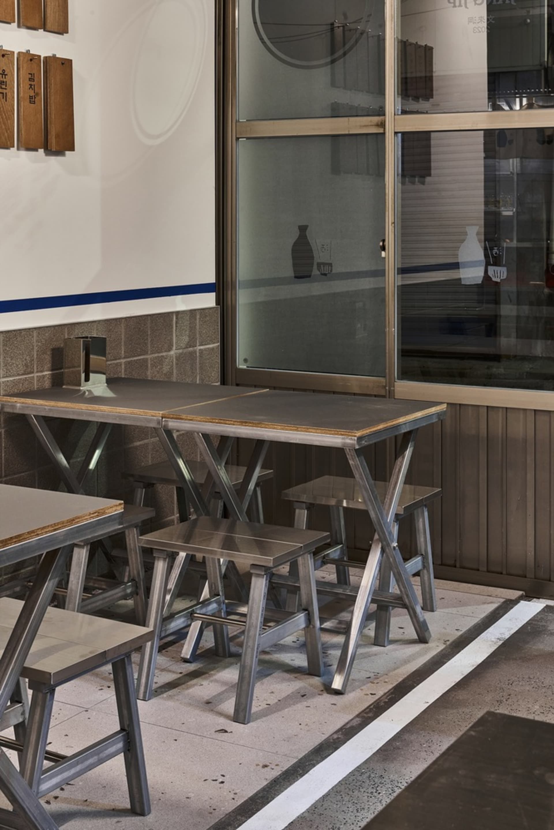 A modern dining area with a metal table and wooden chairs, surrounded by a window allowing natural light to enter
